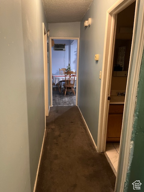 Hall with dark colored carpet, a textured ceiling, a wall mounted AC, and sink