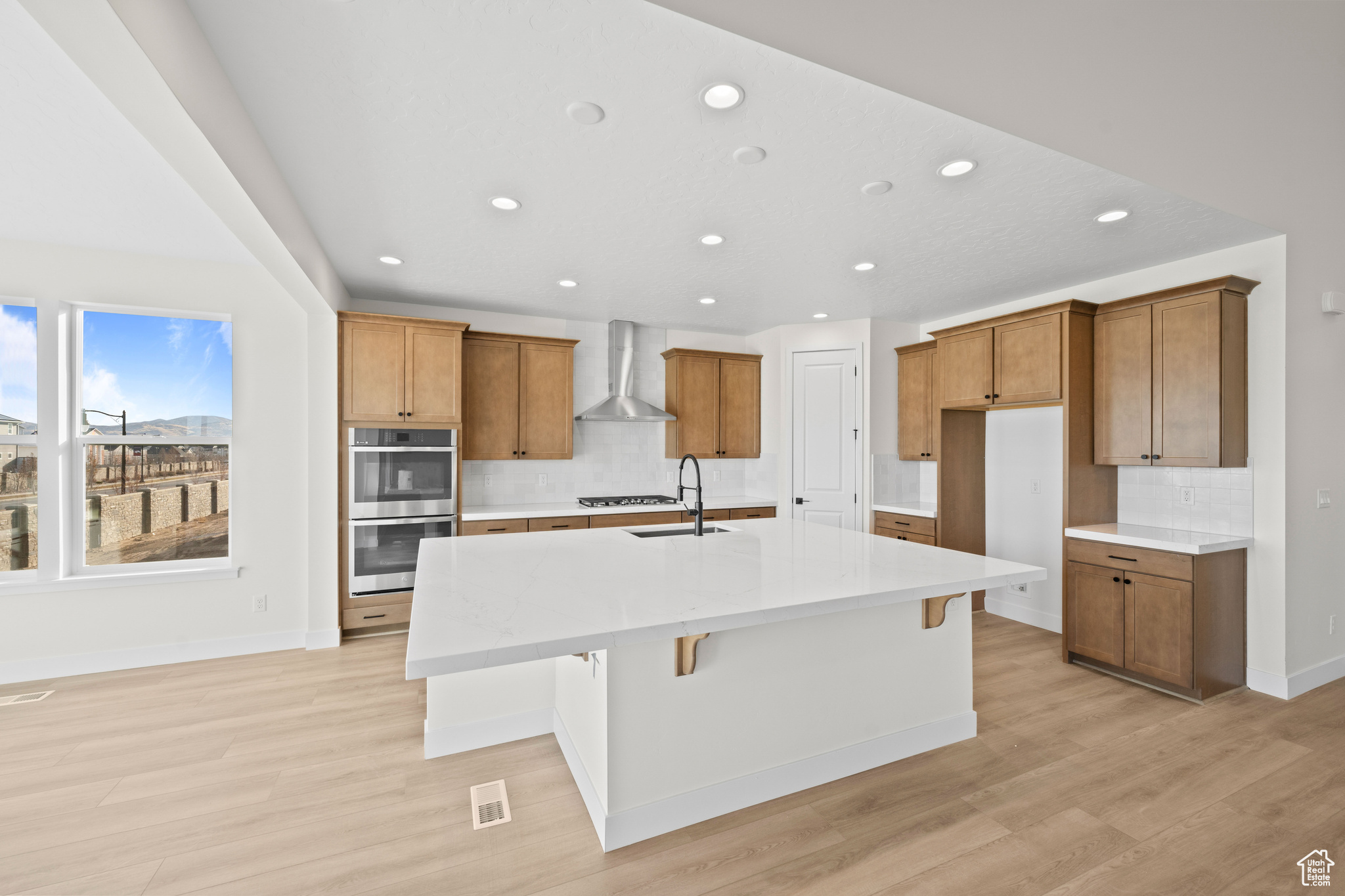 Kitchen featuring a breakfast bar, a large island with sink, double oven, and wall chimney exhaust hood