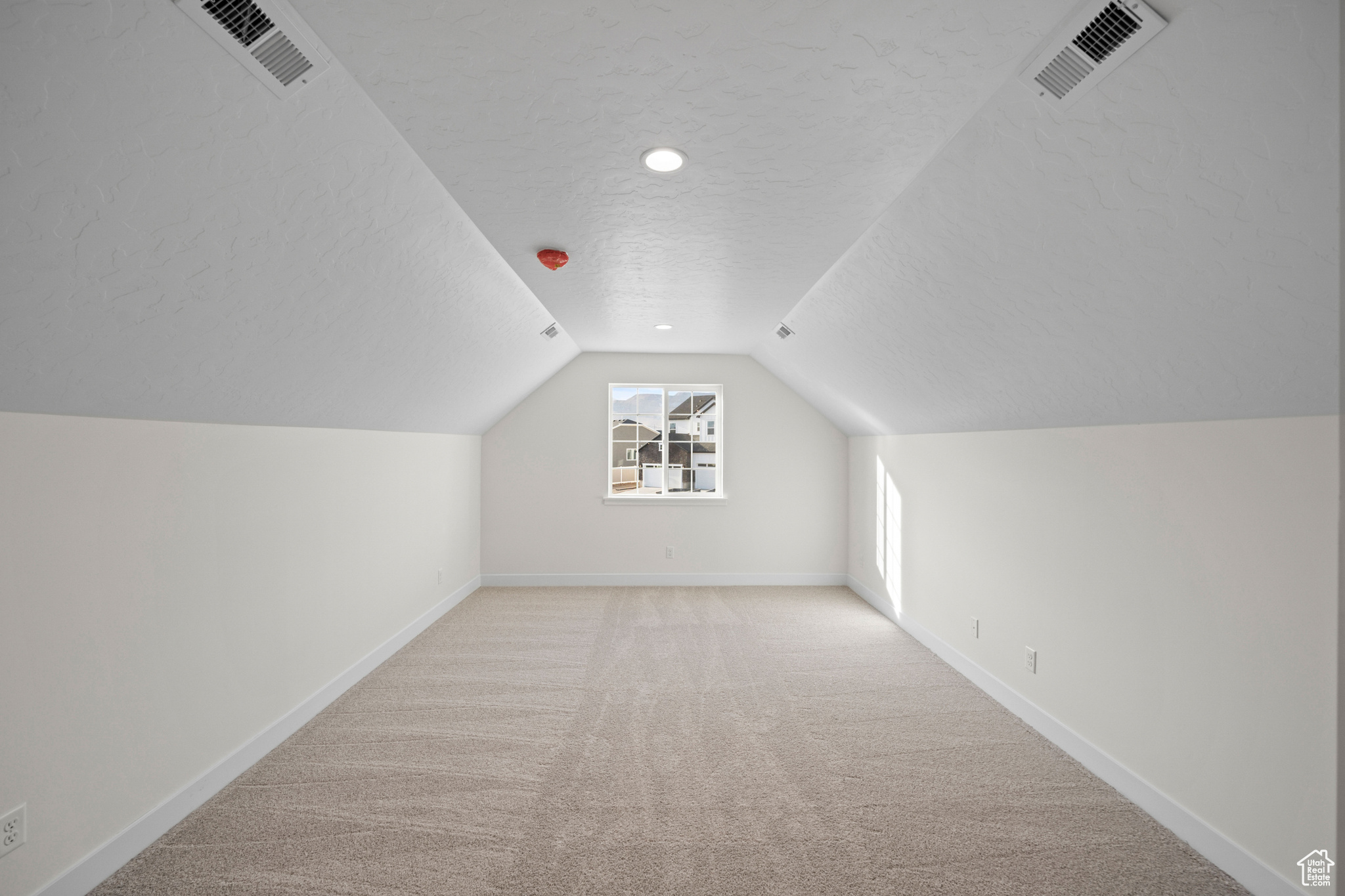 Additional living space with vaulted ceiling, light colored carpet, and a textured ceiling