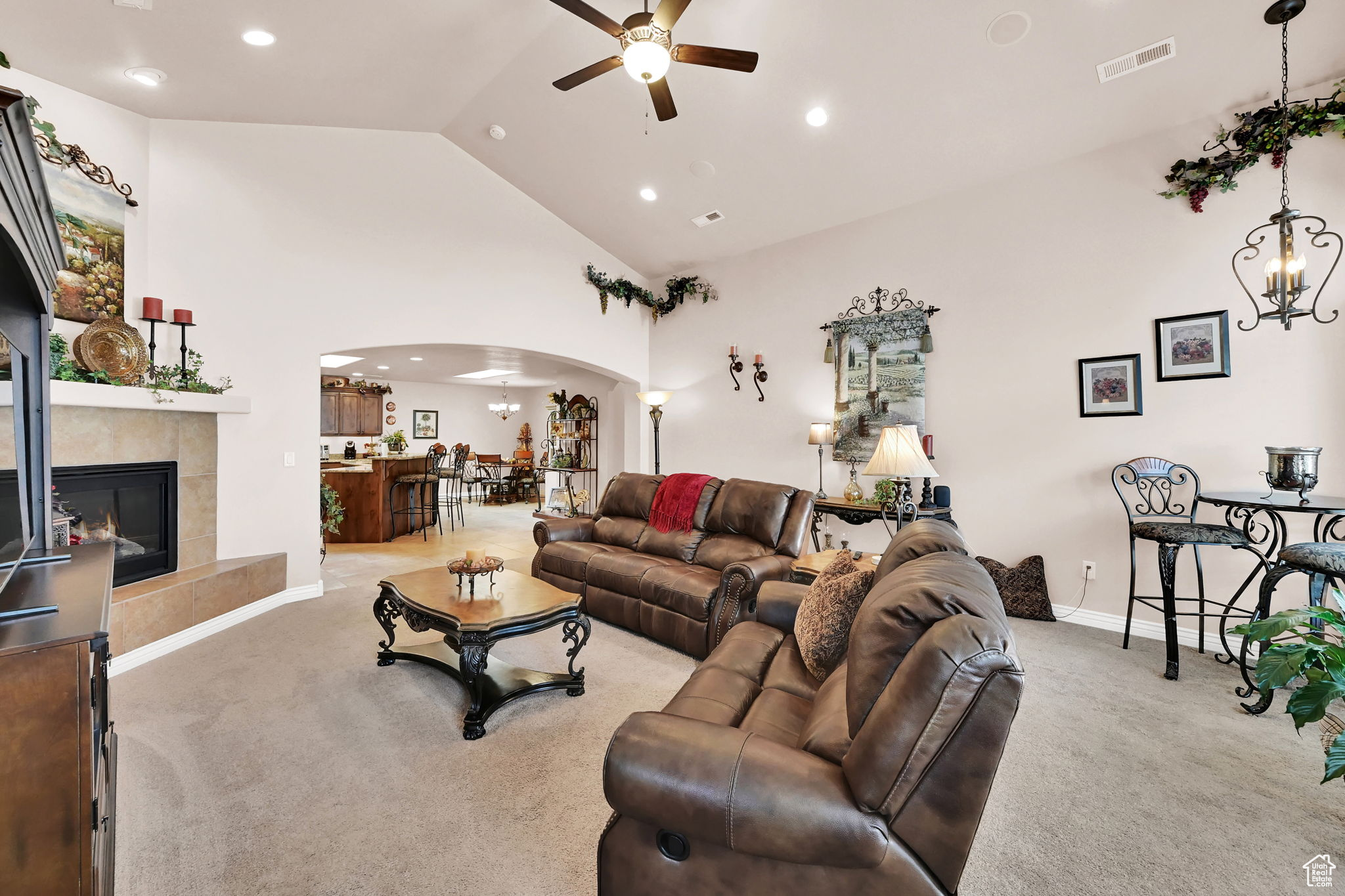 Living room featuring a tile fireplace, high vaulted ceiling, light colored carpet, and ceiling fan with notable chandelier