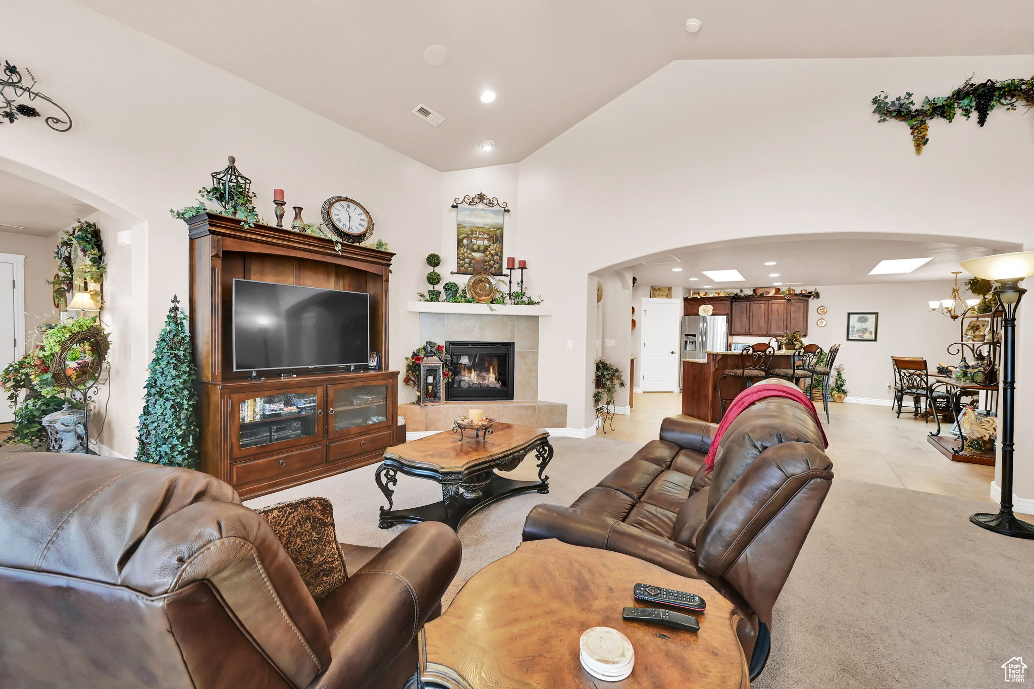 Carpeted living room with a tile fireplace, vaulted ceiling, and an inviting chandelier