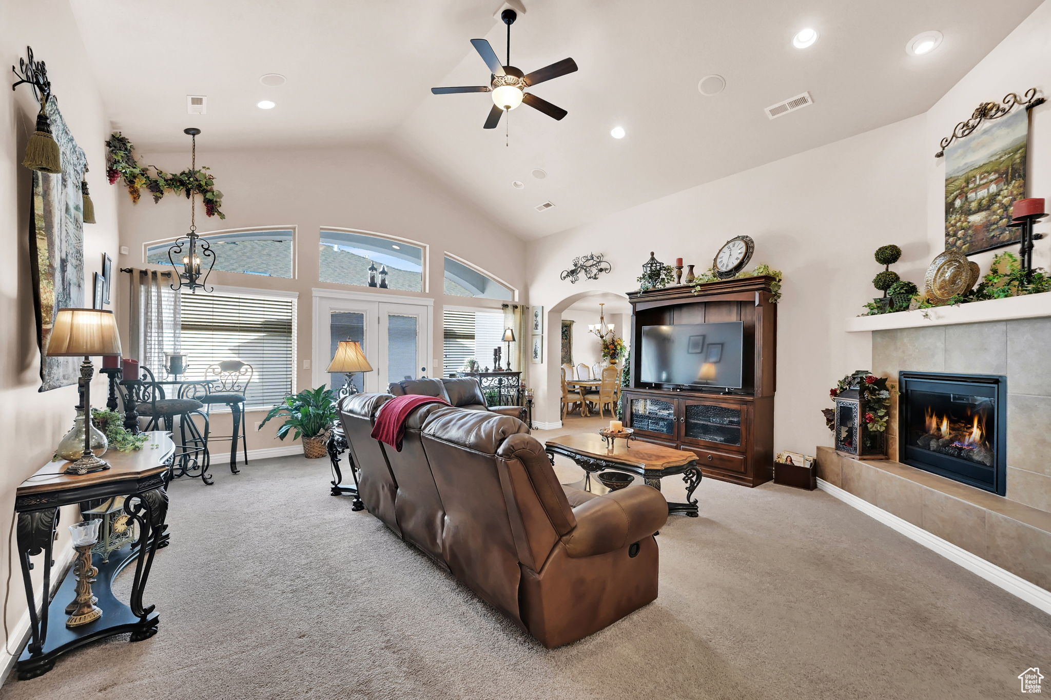 Living room featuring ceiling fan with notable chandelier, french doors, light carpet, and a tiled fireplace