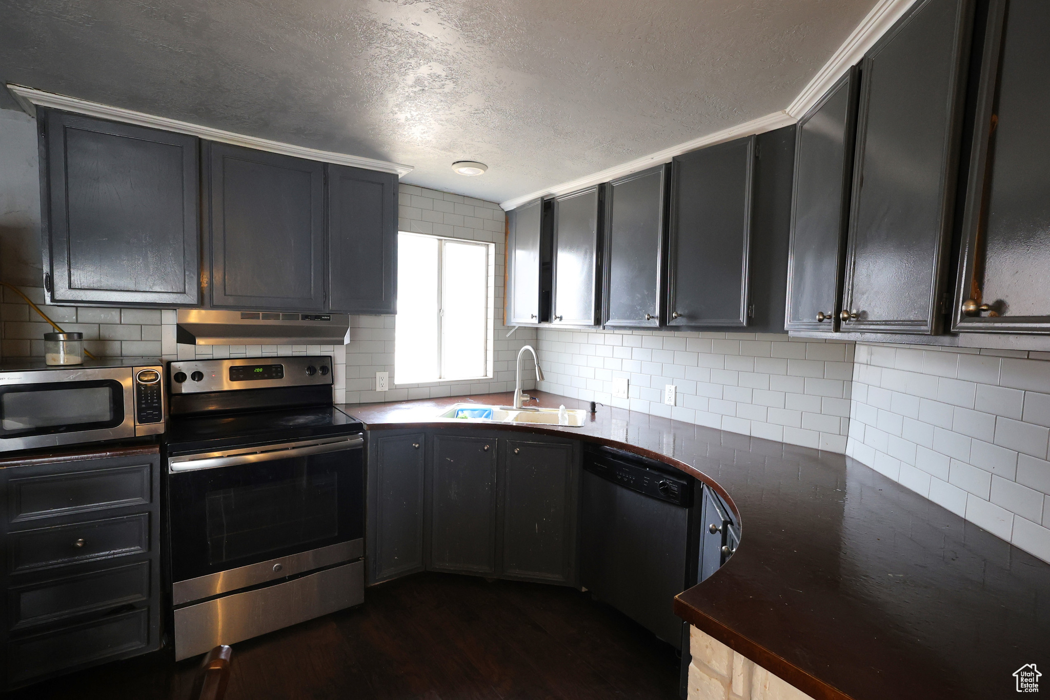 Kitchen featuring tasteful backsplash, ornamental molding, stainless steel appliances, dark wood-type flooring, and sink