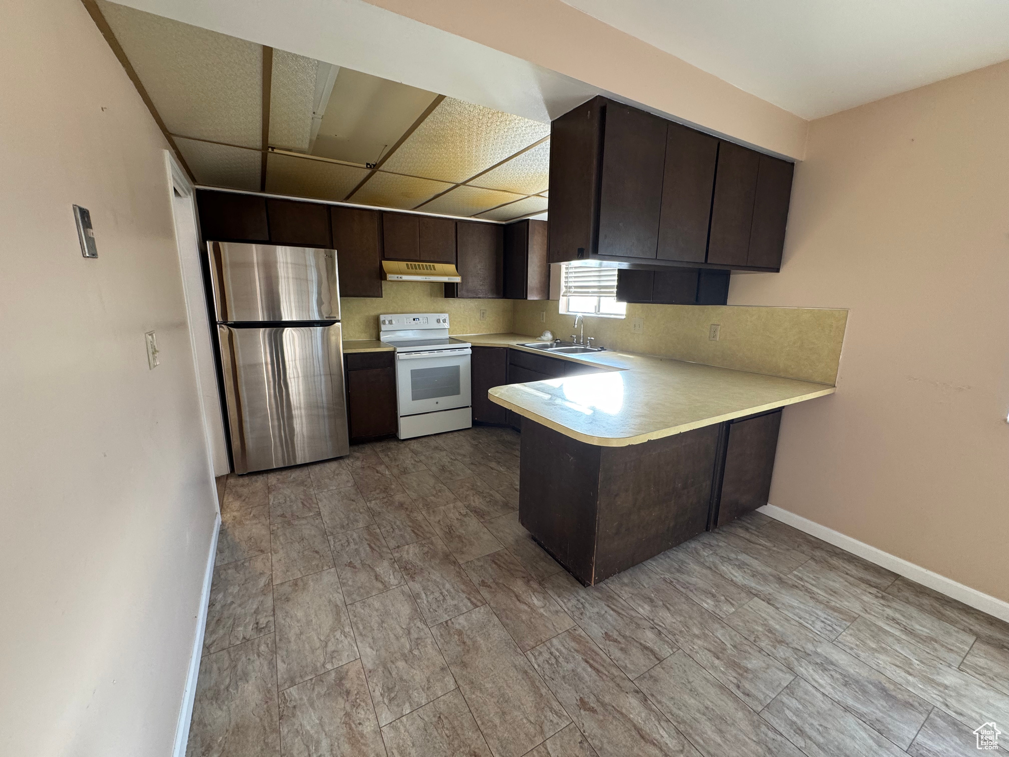 Kitchen featuring sink, white electric stove, kitchen peninsula, stainless steel fridge, and dark brown cabinets