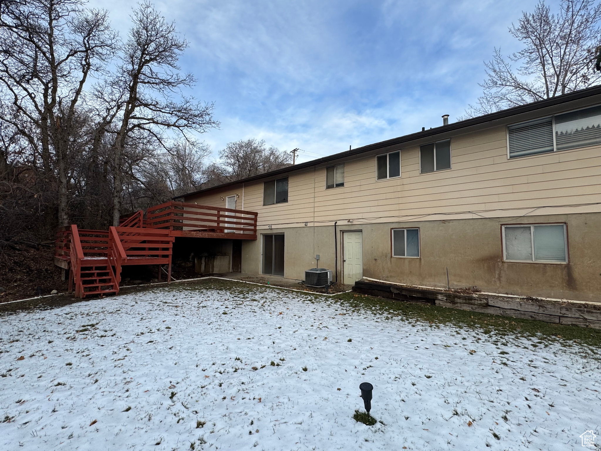 Snow covered back of property with cooling unit and a deck