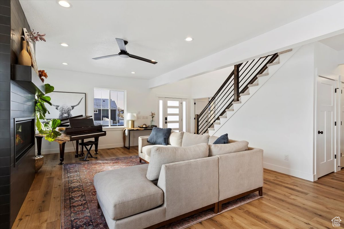 Living room with ceiling fan, a large fireplace, and light wood-type flooring