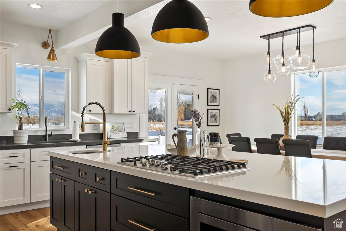 Kitchen with white cabinetry, sink, stainless steel gas cooktop, light hardwood / wood-style flooring, and pendant lighting