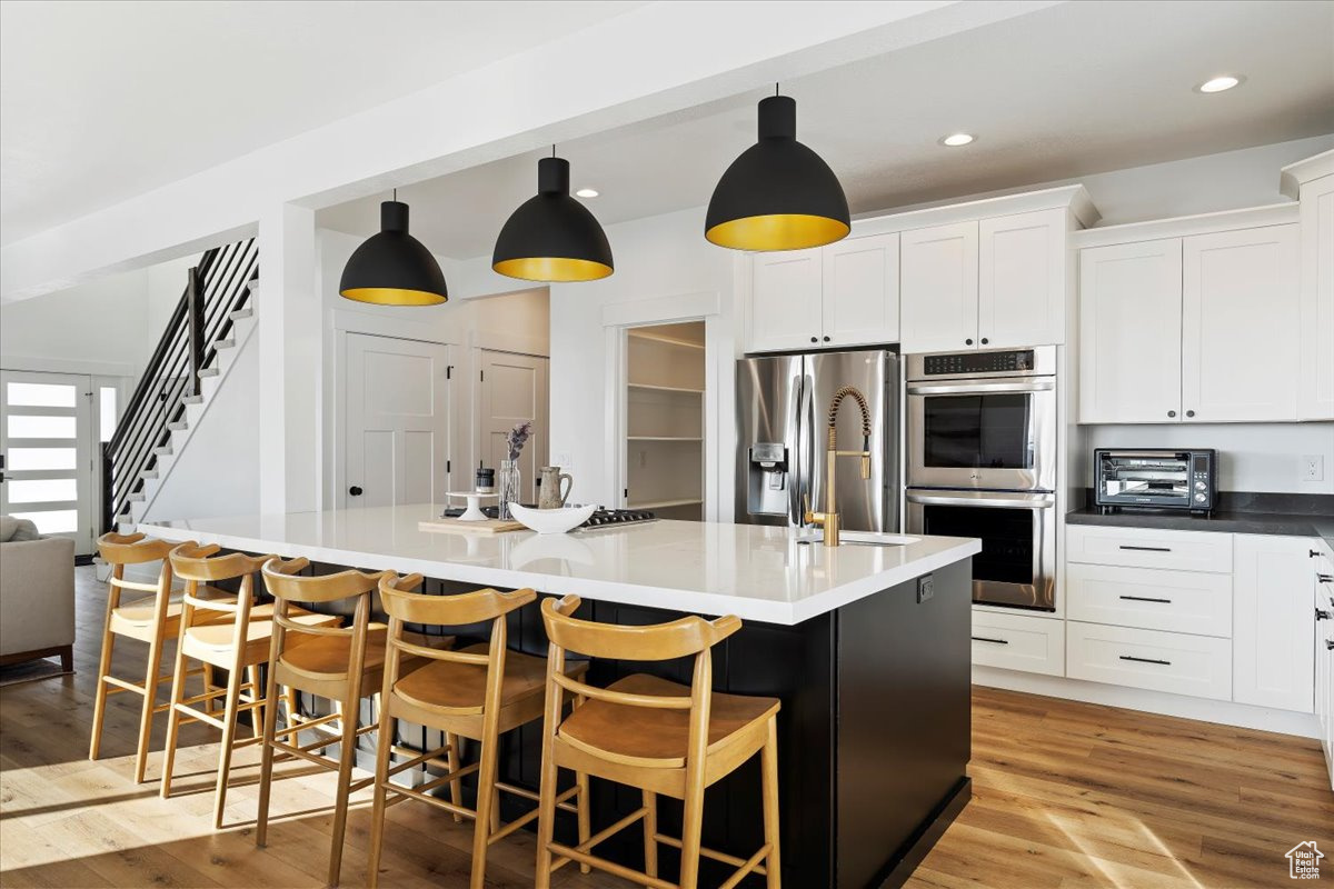 Kitchen featuring light hardwood / wood-style flooring, stainless steel appliances, hanging light fixtures, and an island with sink