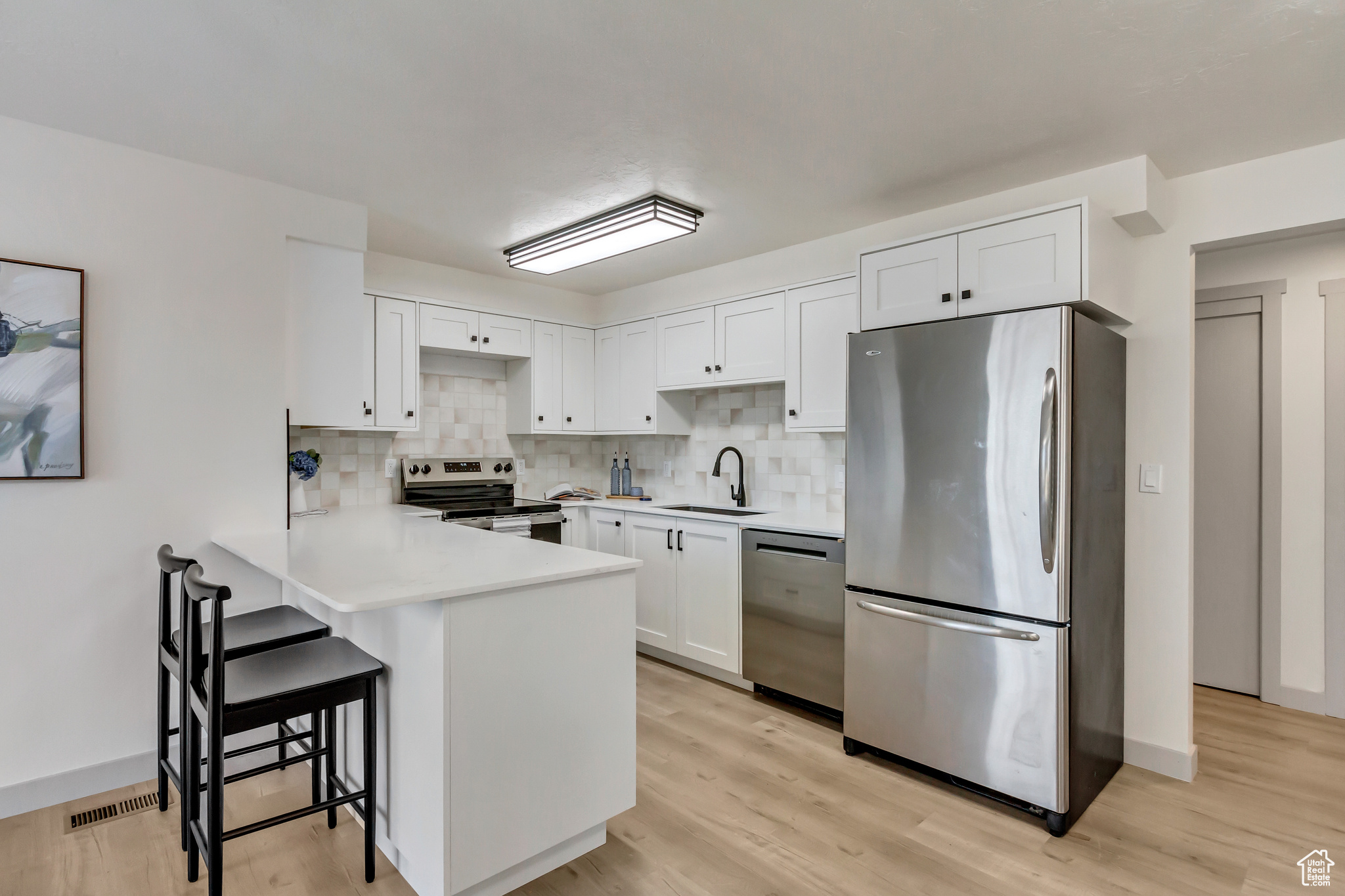 Kitchen with white cabinetry, sink, light hardwood / wood-style flooring, backsplash, and appliances with stainless steel finishes