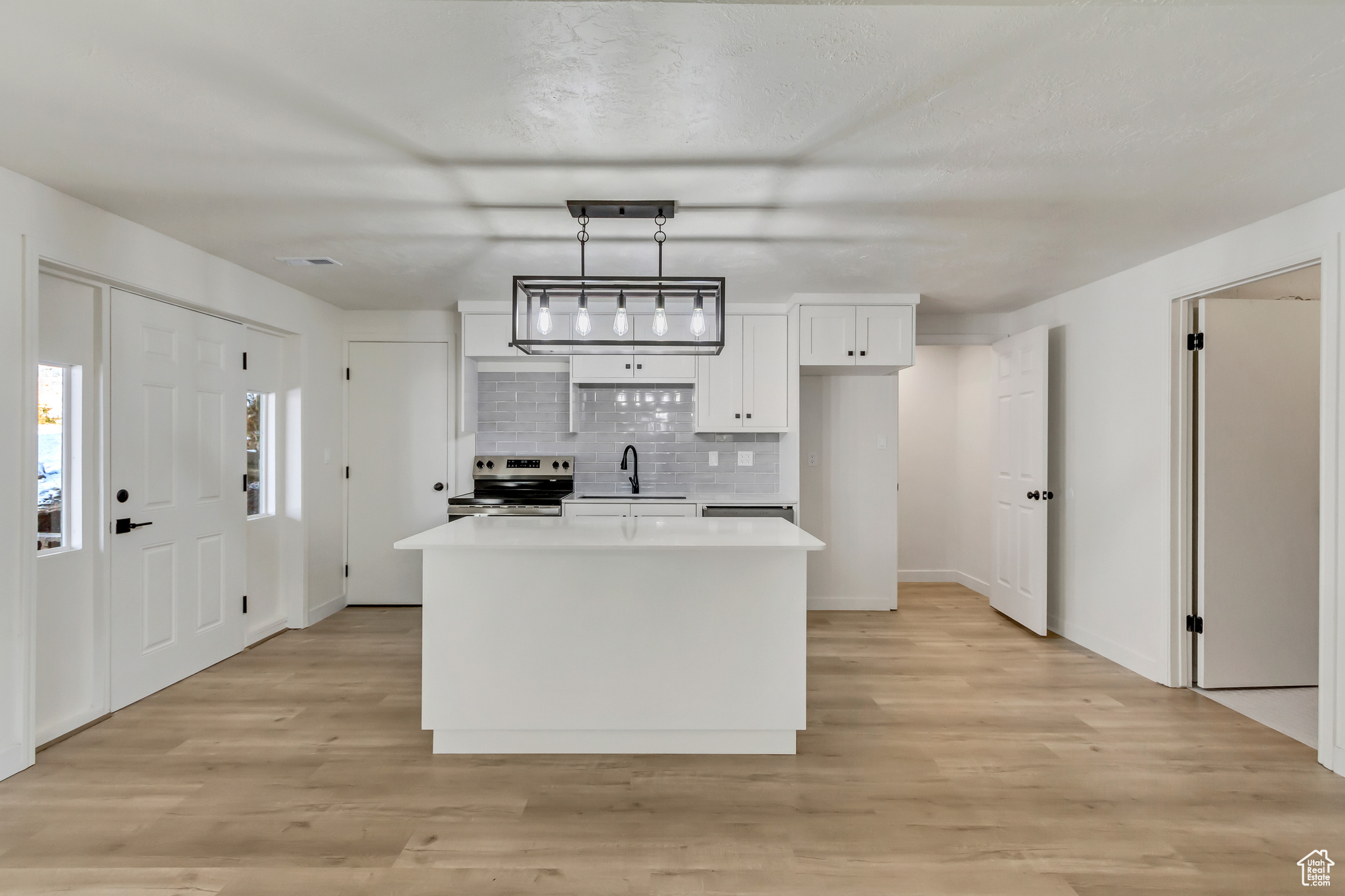 Kitchen with stainless steel range with electric cooktop, white cabinets, hanging light fixtures, light wood-type flooring, and a kitchen island