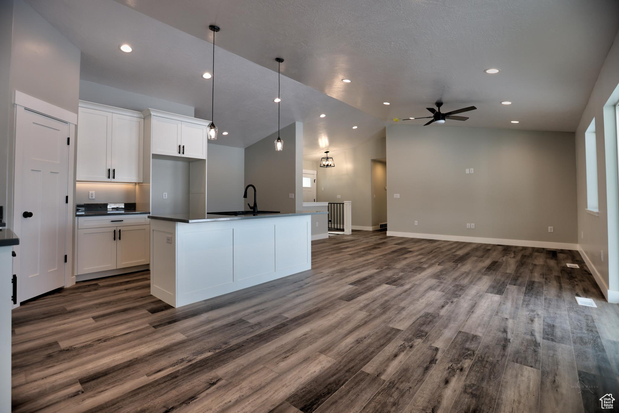 Kitchen with ceiling fan, dark hardwood / wood-style flooring, white cabinetry, and a kitchen island with sink