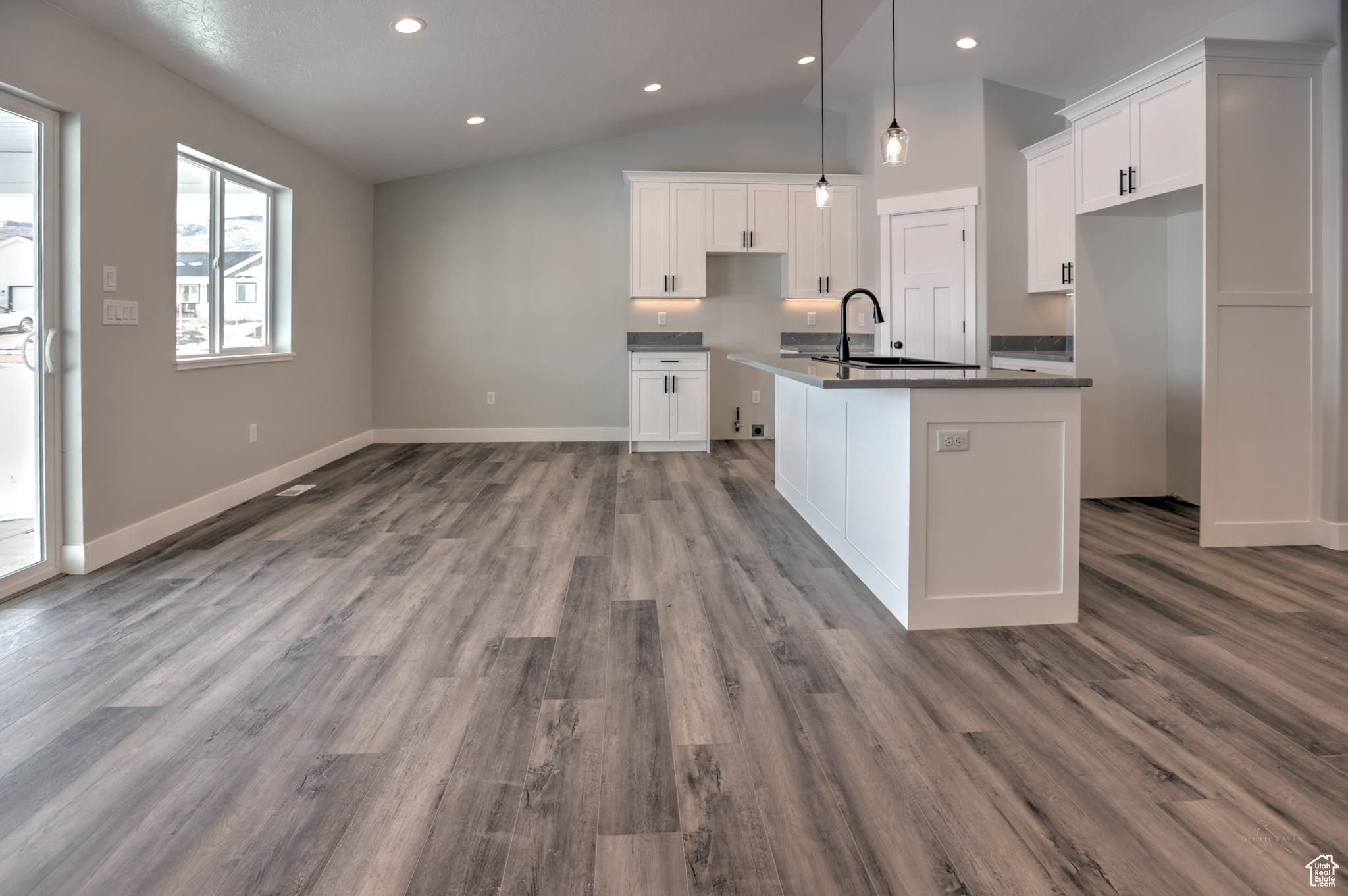 Kitchen featuring white cabinetry, a center island with sink, lofted ceiling, and light wood-type flooring