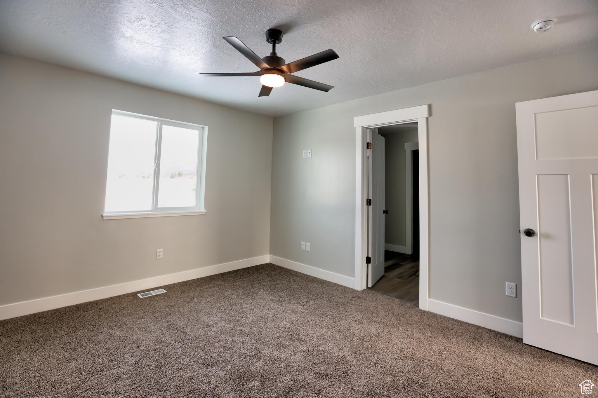 Master bedroom with a textured ceiling, dark carpet, and ceiling fan