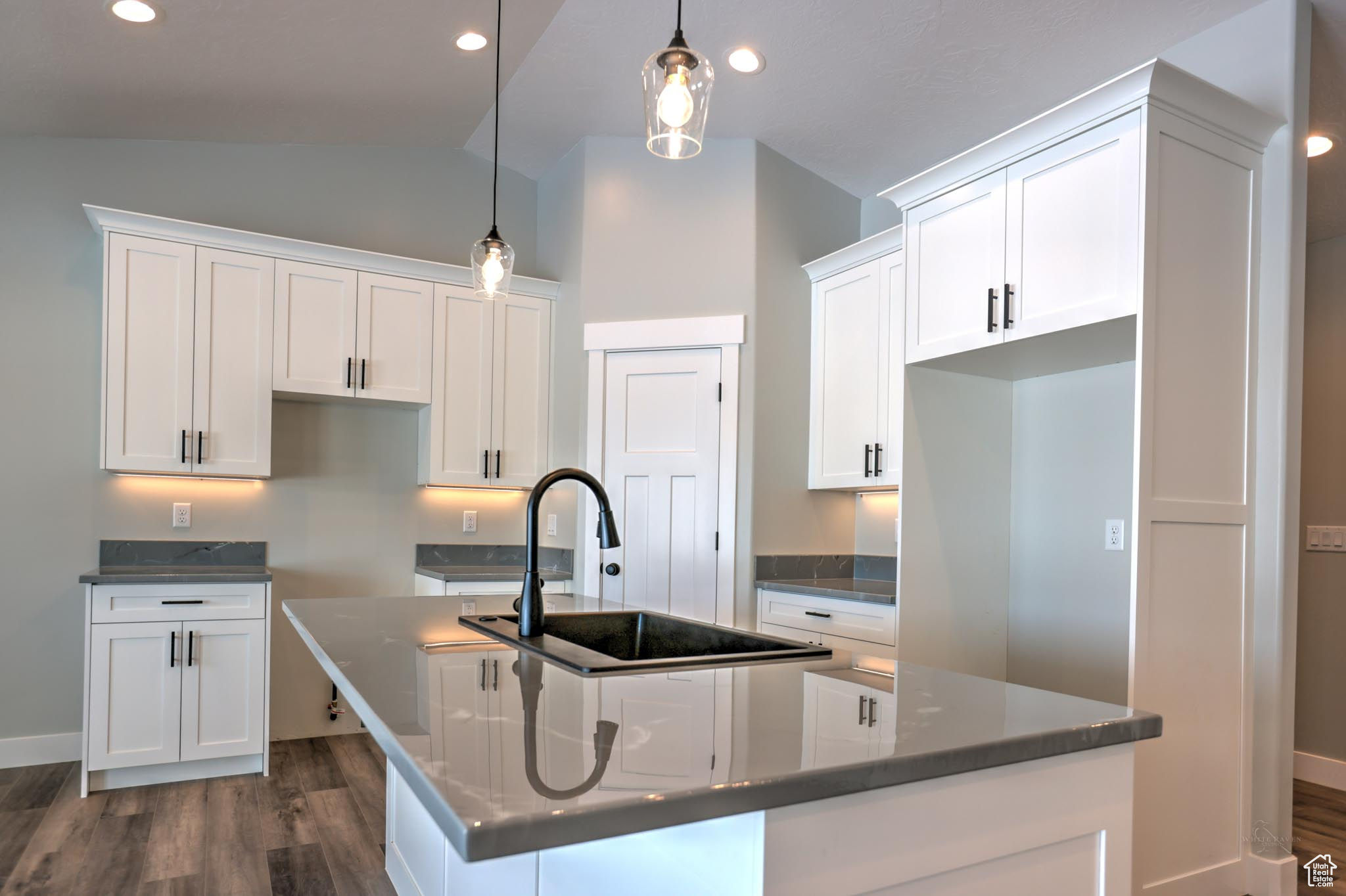 Kitchen with a center island with sink, white cabinets, hanging light fixtures, and lofted ceiling