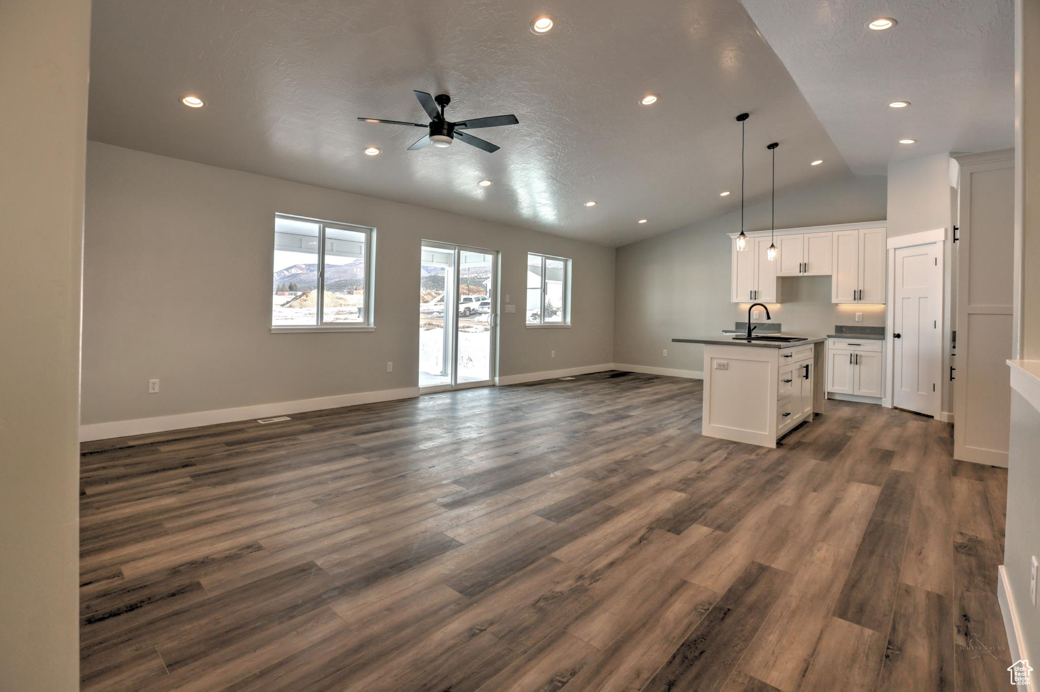 Kitchen with pendant lighting, vaulted ceiling, dark hardwood / wood-style floors, an island with sink, and white cabinetry