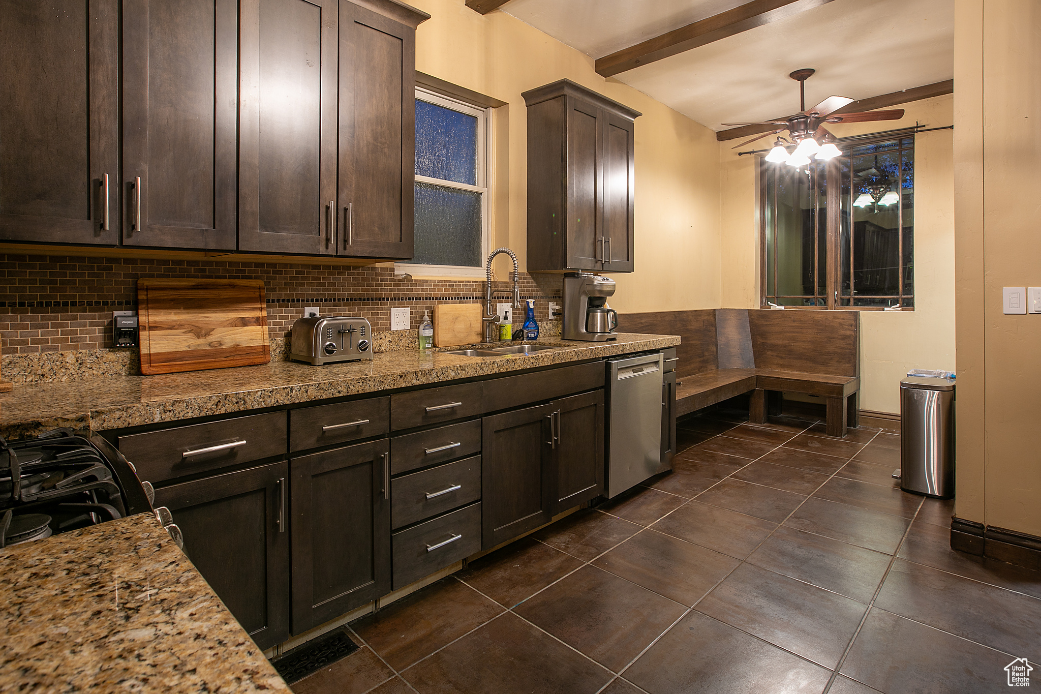 Kitchen with stainless steel dishwasher, dark brown cabinetry, sink, and tasteful backsplash