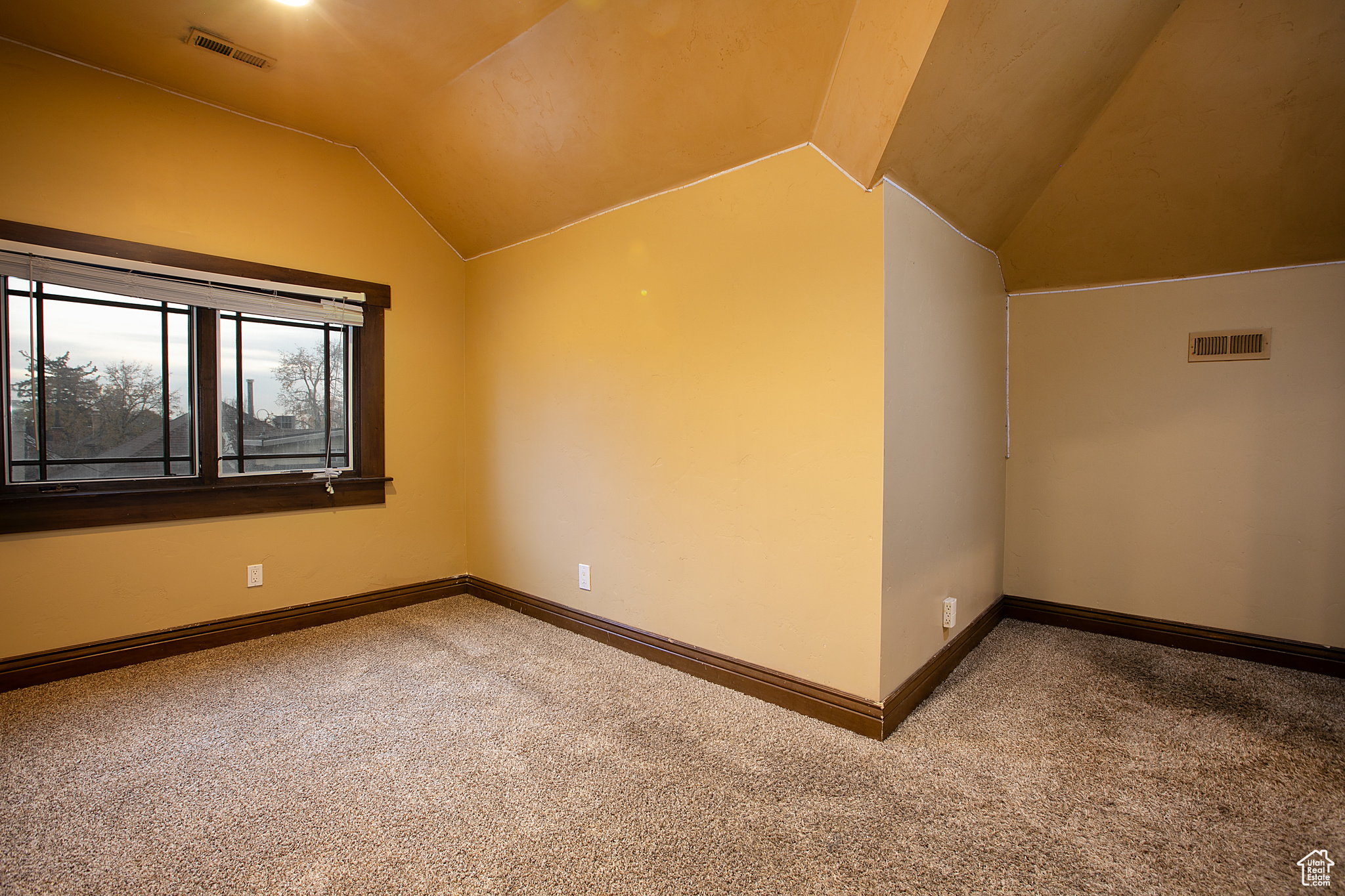 Carpeted empty room featuring vaulted ceiling