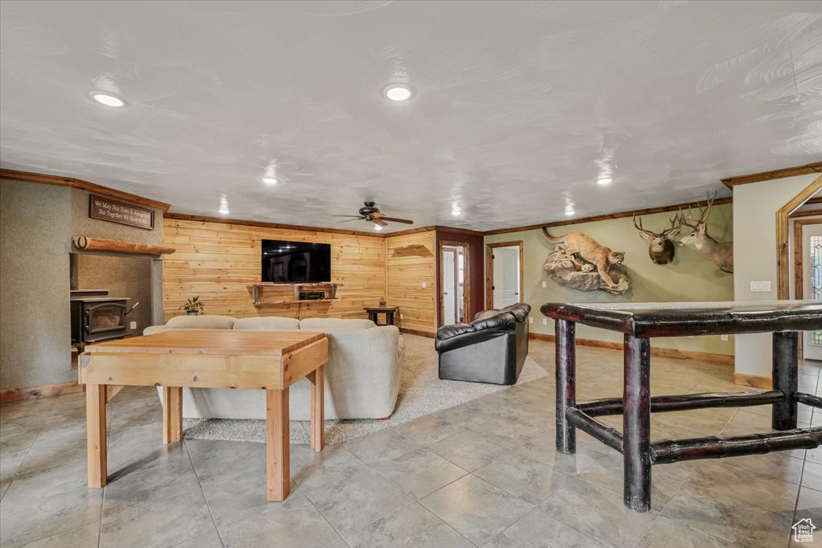 Living room featuring ceiling fan, wood walls, a wood stove, and crown molding