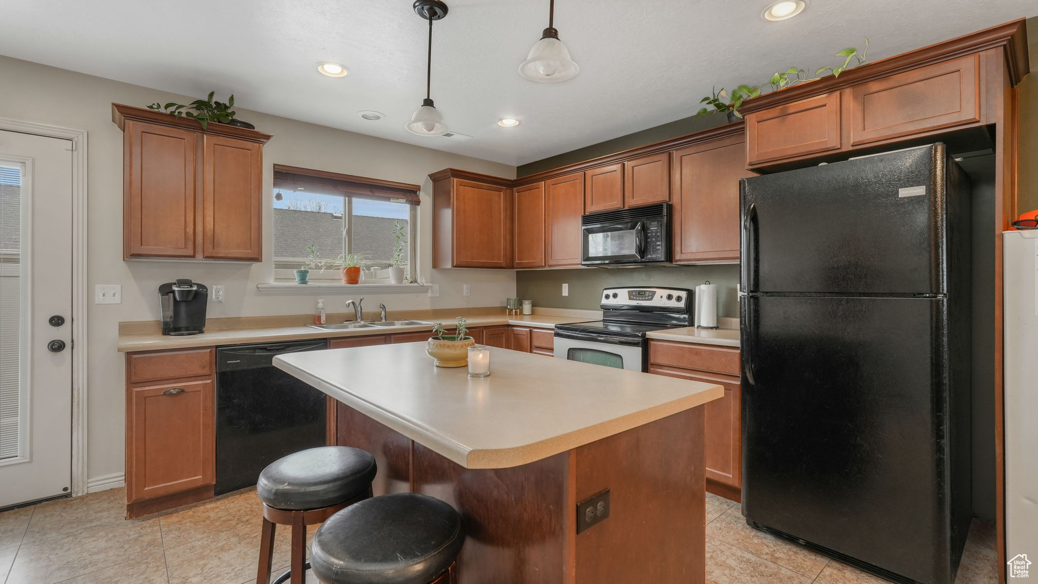 Kitchen featuring a breakfast bar, sink, black appliances, pendant lighting, and a kitchen island