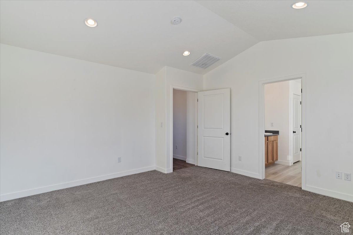 Unfurnished bedroom featuring light carpet, connected bathroom, and vaulted ceiling