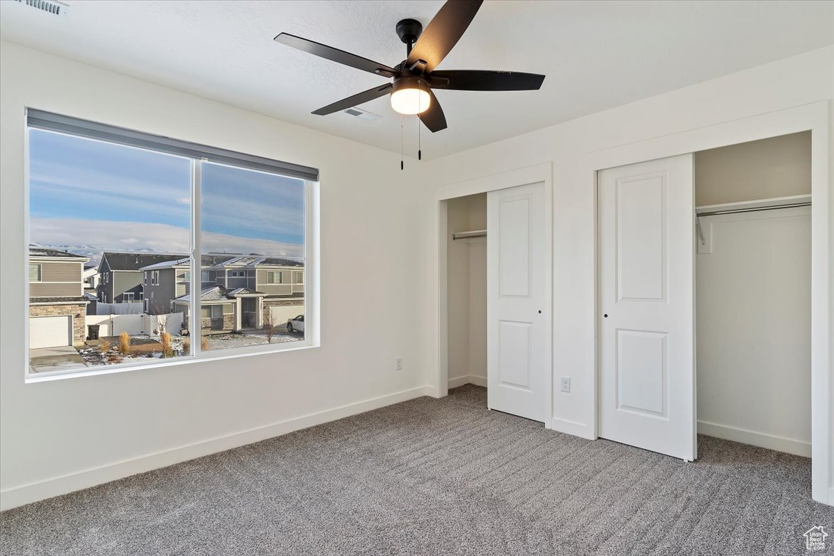 Unfurnished bedroom with multiple windows, ceiling fan, carpet, and two closets