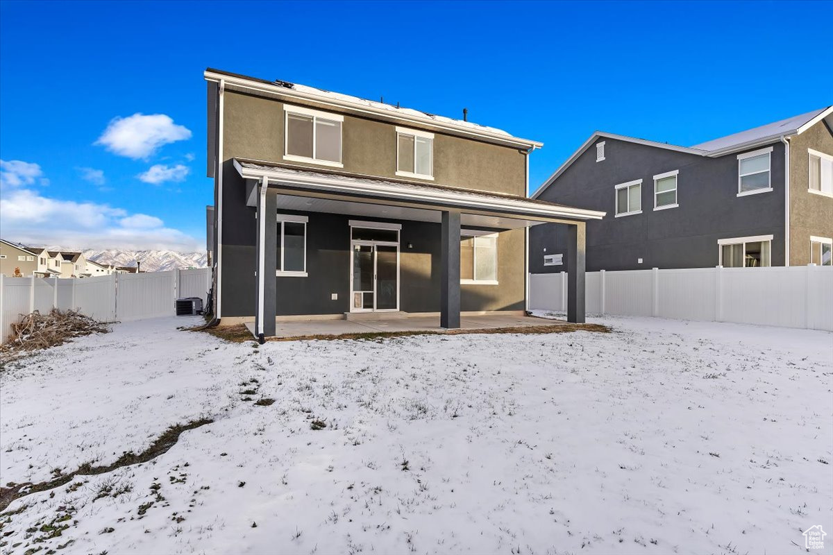 Snow covered rear of property featuring central air condition unit and a patio area