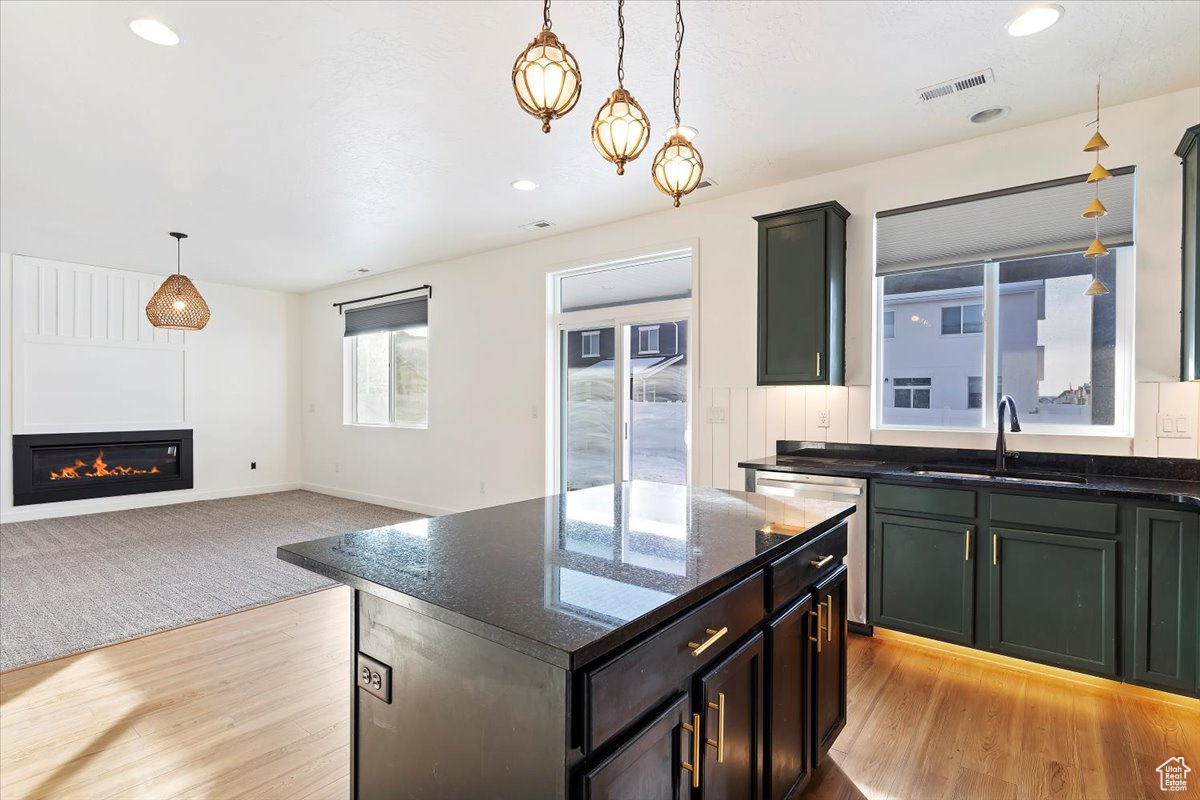 Kitchen featuring light wood-type flooring, sink, pendant lighting, dark stone countertops, and a kitchen island