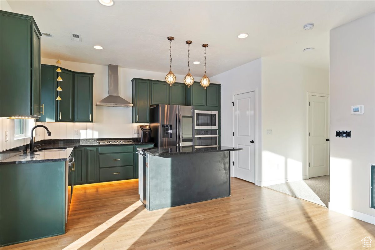 Kitchen featuring sink, wall chimney exhaust hood, stainless steel appliances, light hardwood / wood-style flooring, and a kitchen island