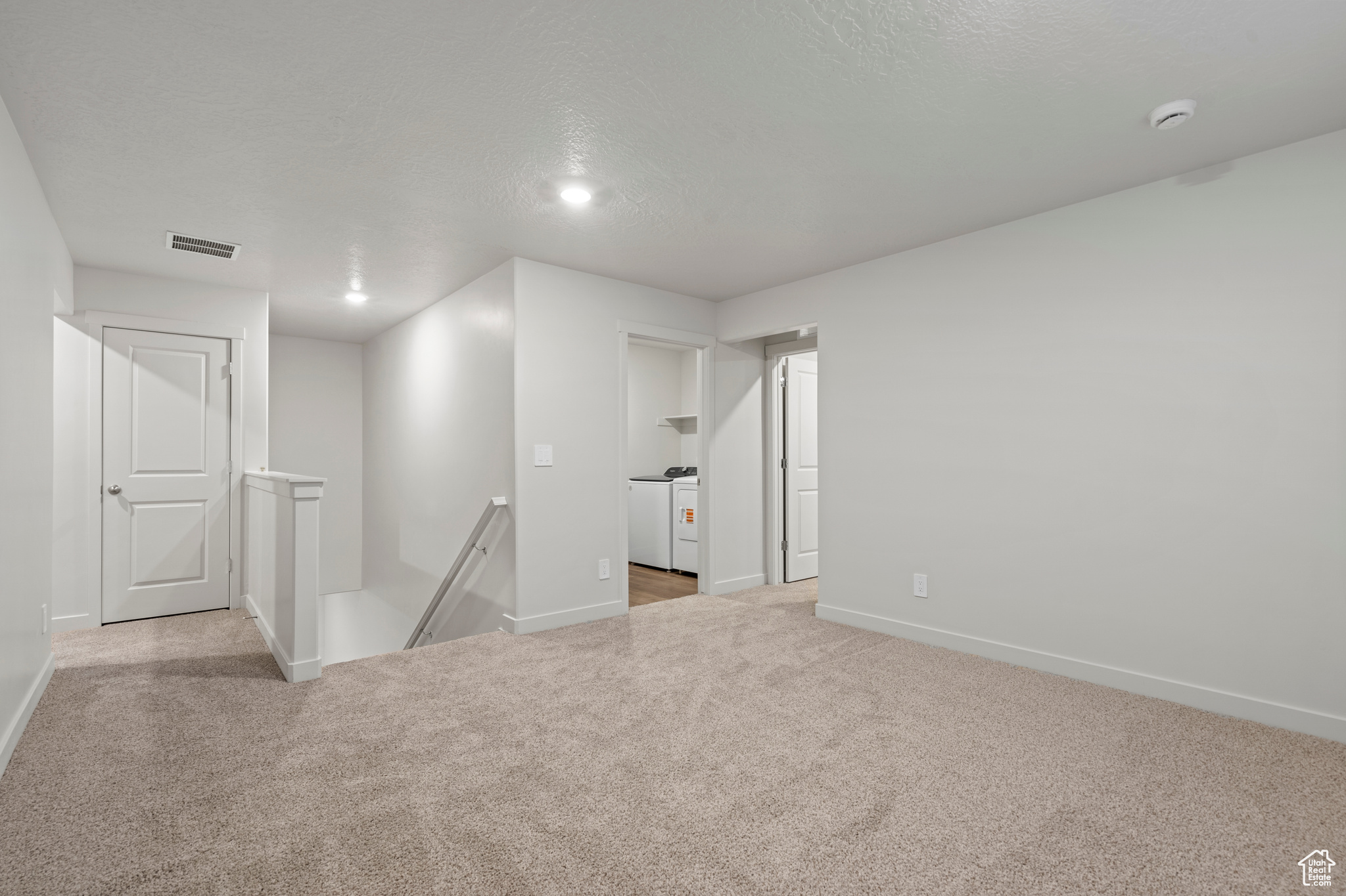 Carpeted empty room featuring a textured ceiling and independent washer and dryer