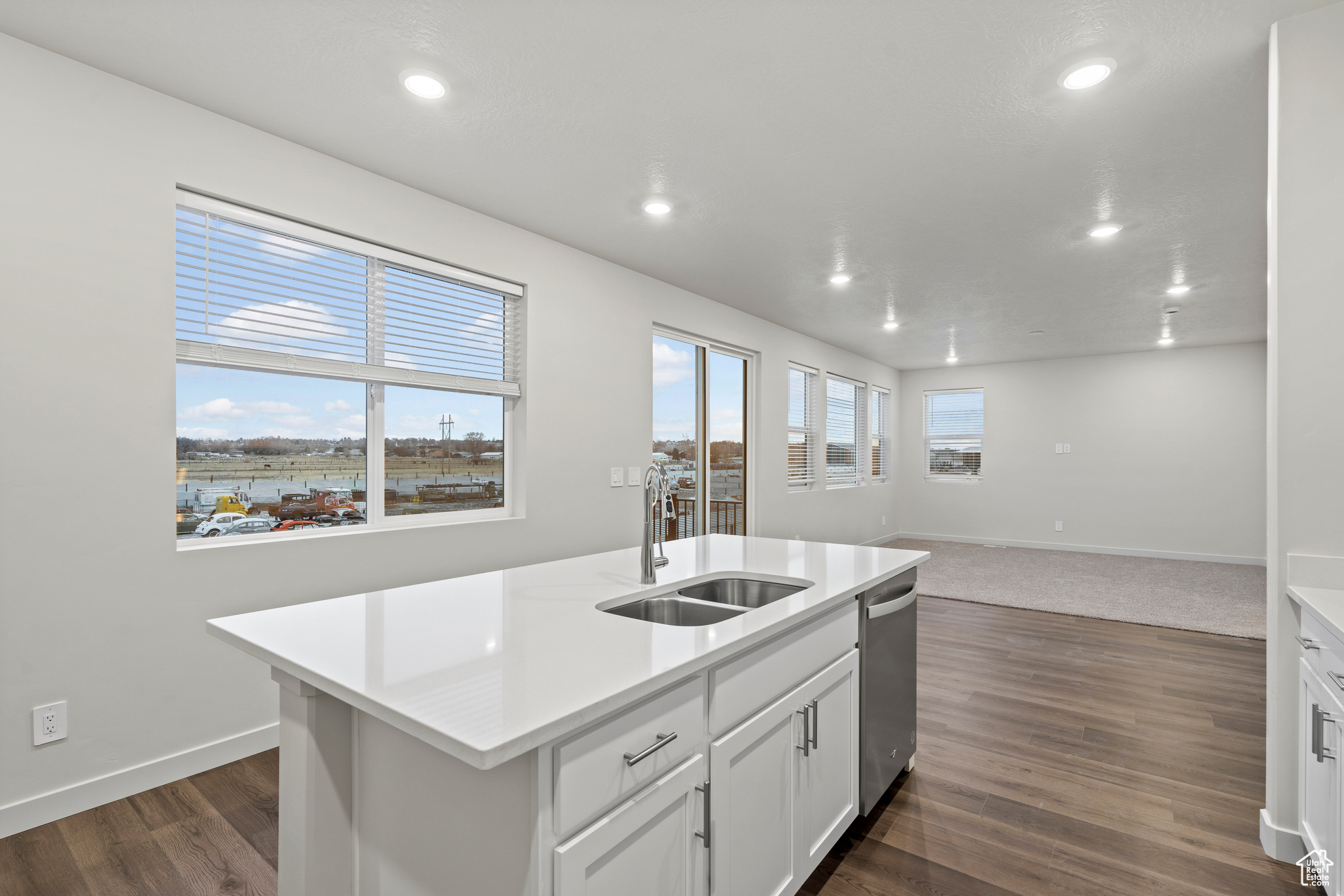 Kitchen featuring sink, dark wood-type flooring, dishwasher, white cabinetry, and an island with sink