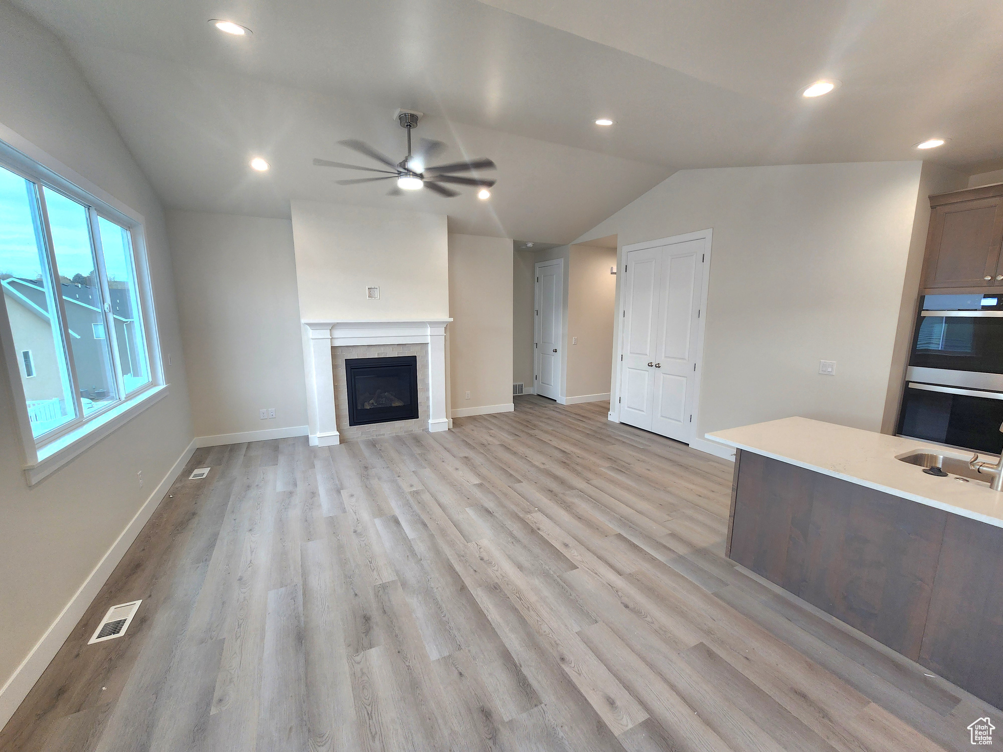 Unfurnished living room featuring a fireplace, light hardwood / wood-style floors, ceiling fan, and lofted ceiling