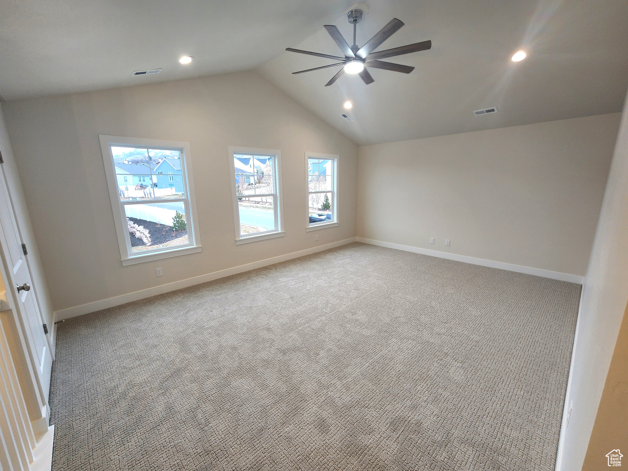 Empty room with ceiling fan, light colored carpet, and vaulted ceiling