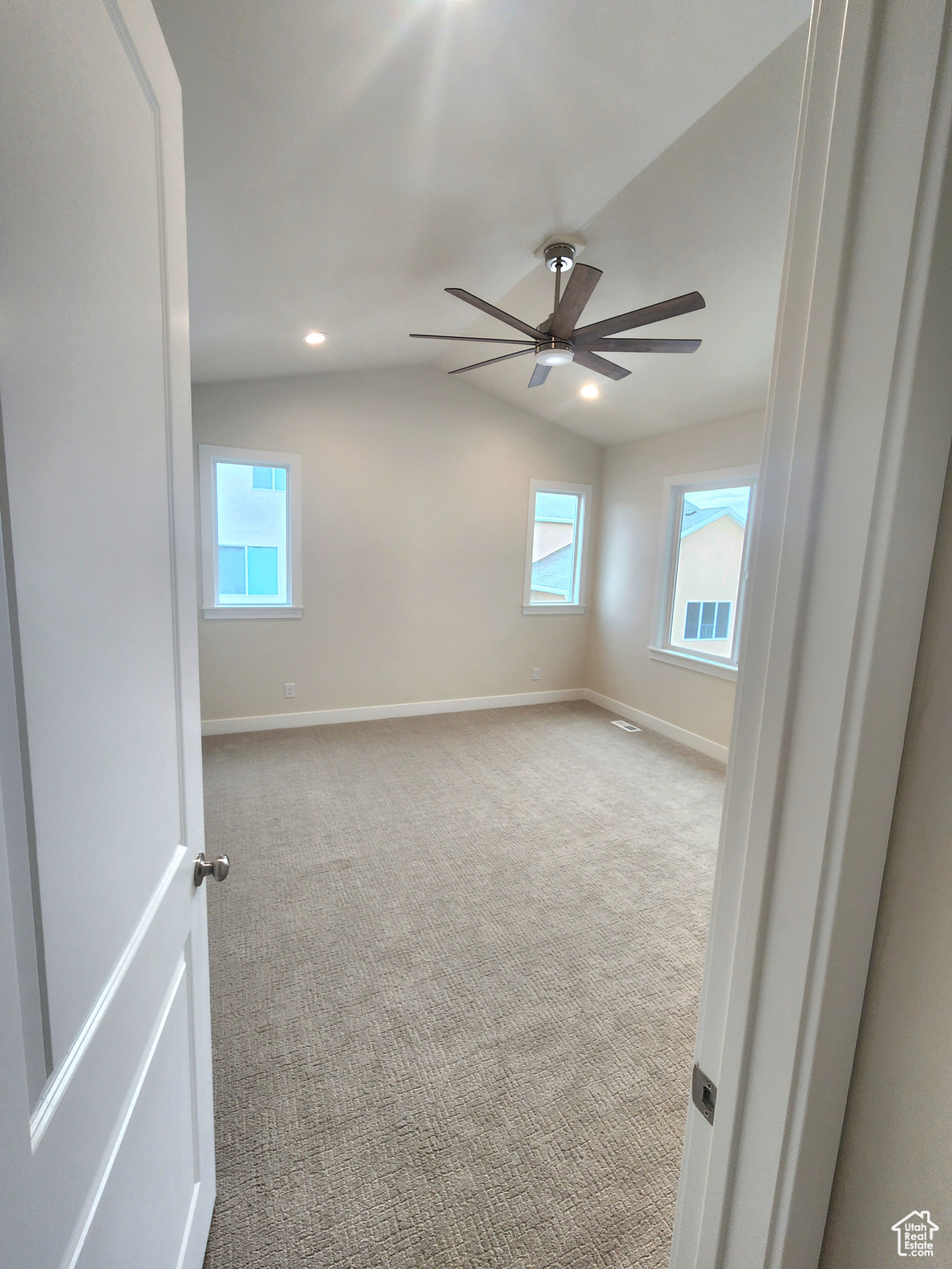 Carpeted empty room with ceiling fan and lofted ceiling