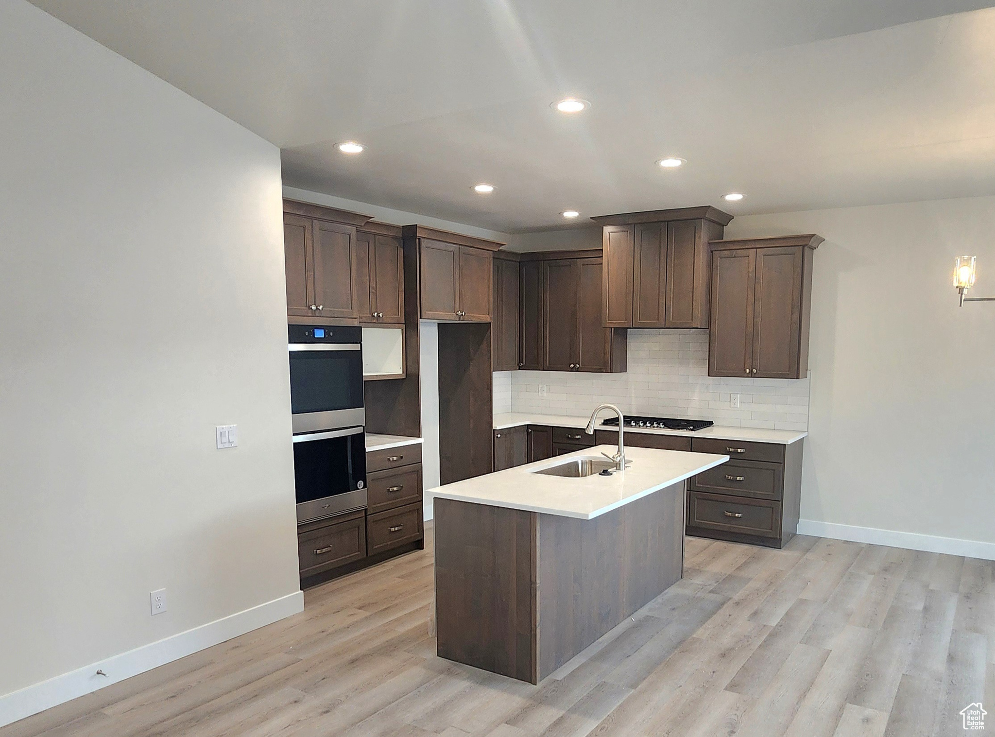 Kitchen with sink, gas stovetop, double oven, light hardwood / wood-style floors, and dark brown cabinets