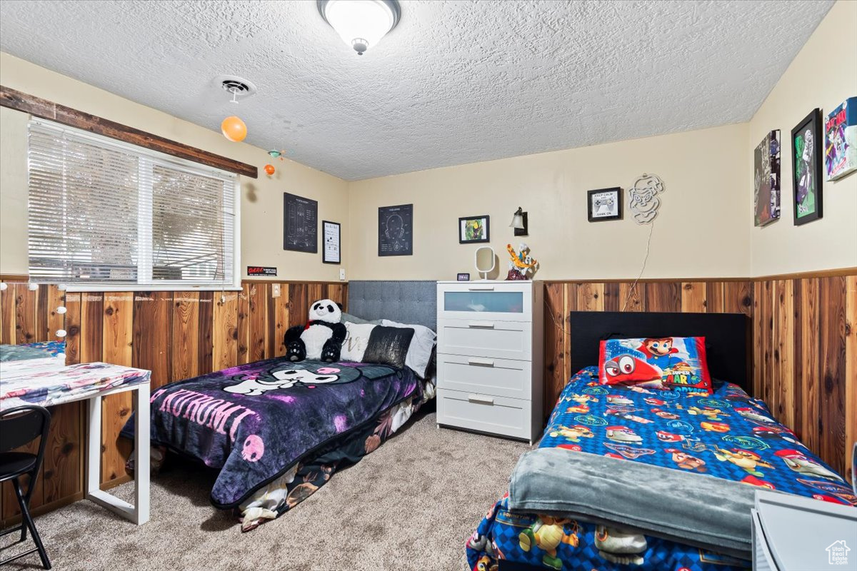 Bedroom featuring light colored carpet, a textured ceiling, and wooden walls