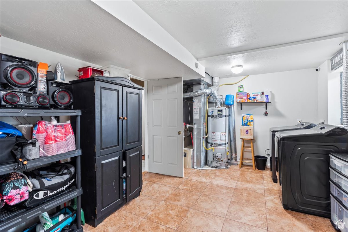 Clothes washing area with cabinets, a textured ceiling, water heater, washing machine and clothes dryer, and light tile patterned flooring