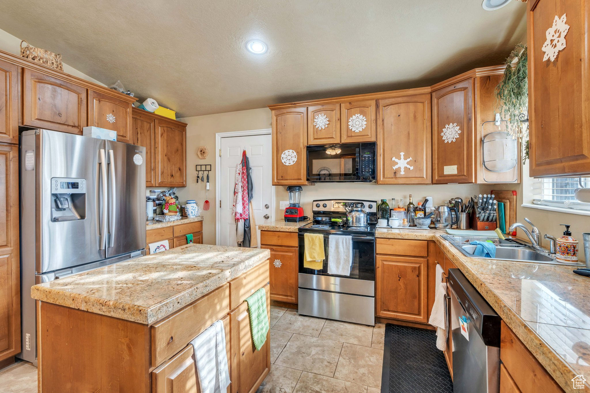 Kitchen featuring appliances with stainless steel finishes, light stone counters, vaulted ceiling, sink, and light tile patterned floors