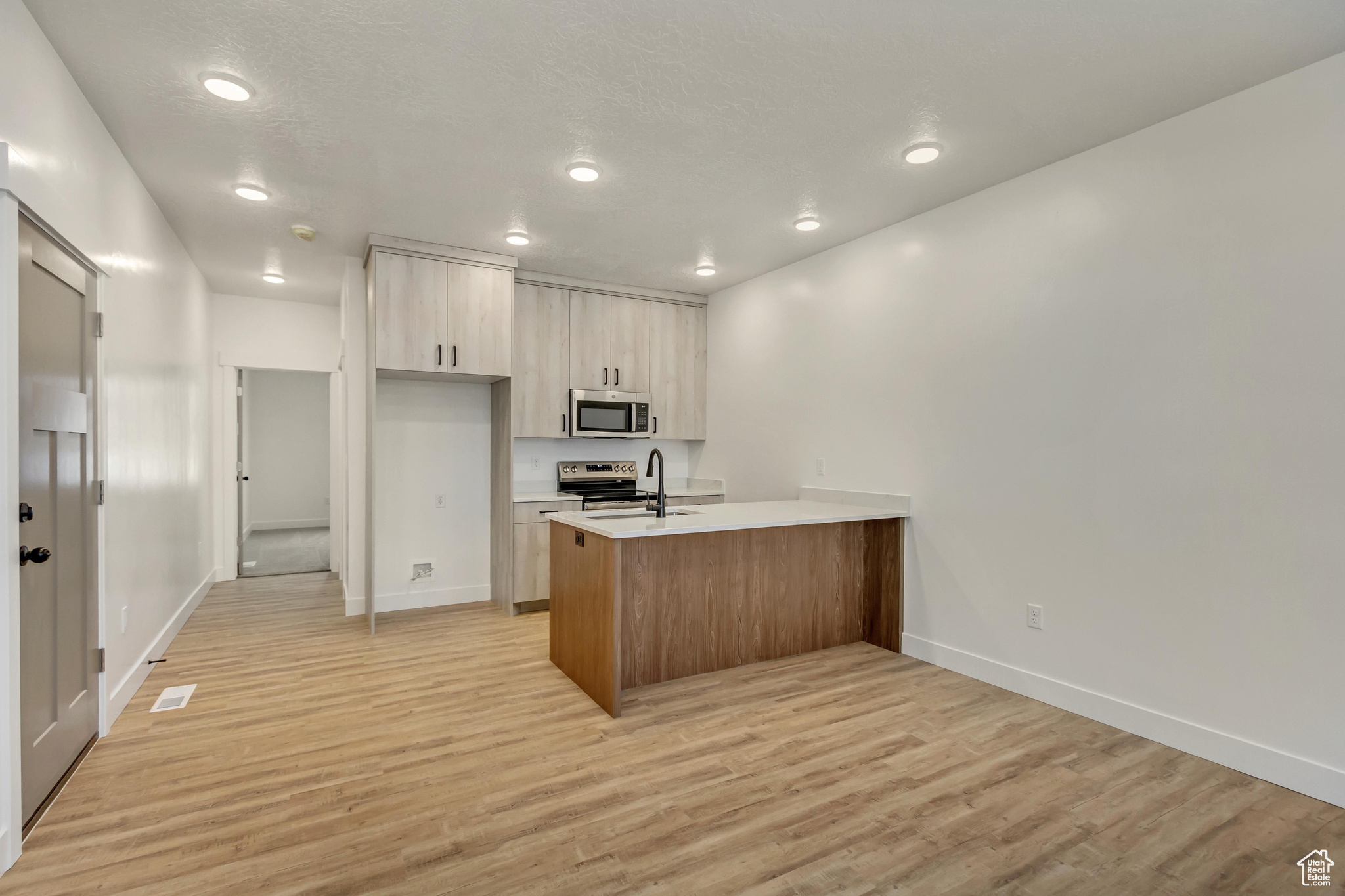 Kitchen featuring light brown cabinets, stainless steel appliances, kitchen peninsula, light hardwood / wood-style floors, and a textured ceiling