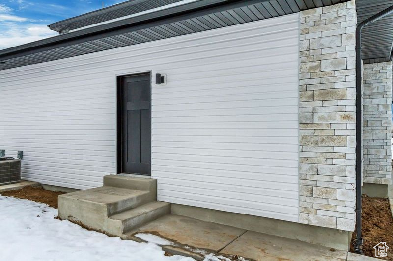 Snow covered property entrance featuring central AC unit