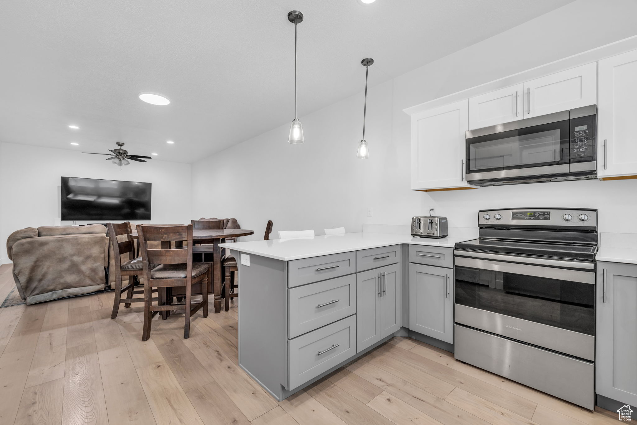 Kitchen with kitchen peninsula, light wood-type flooring, gray cabinetry, stainless steel appliances, and decorative light fixtures