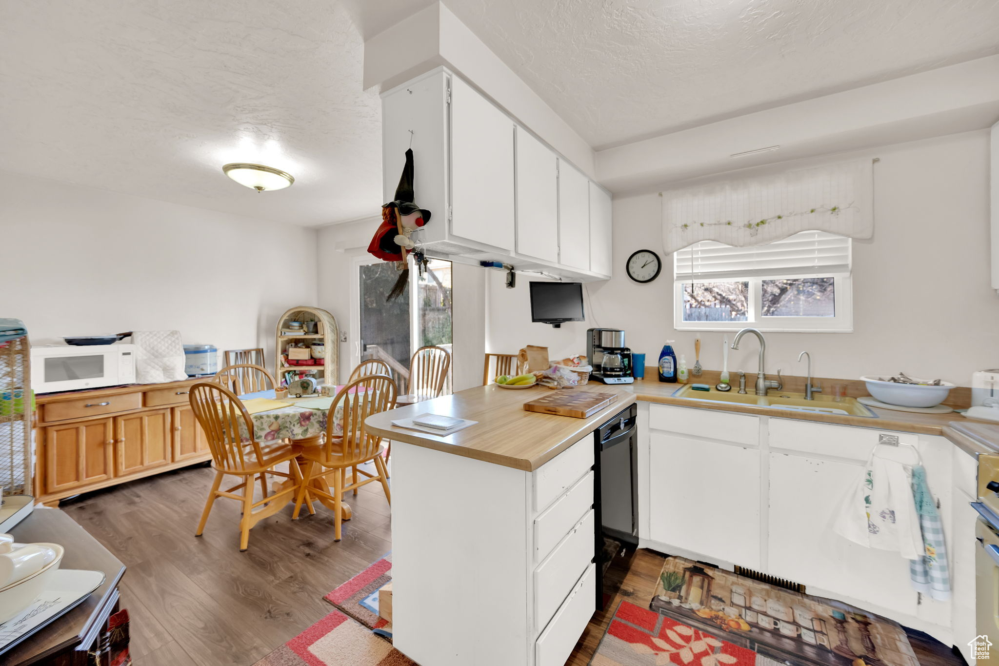 Kitchen with kitchen peninsula, a textured ceiling, dark wood-type flooring, sink, and white cabinets