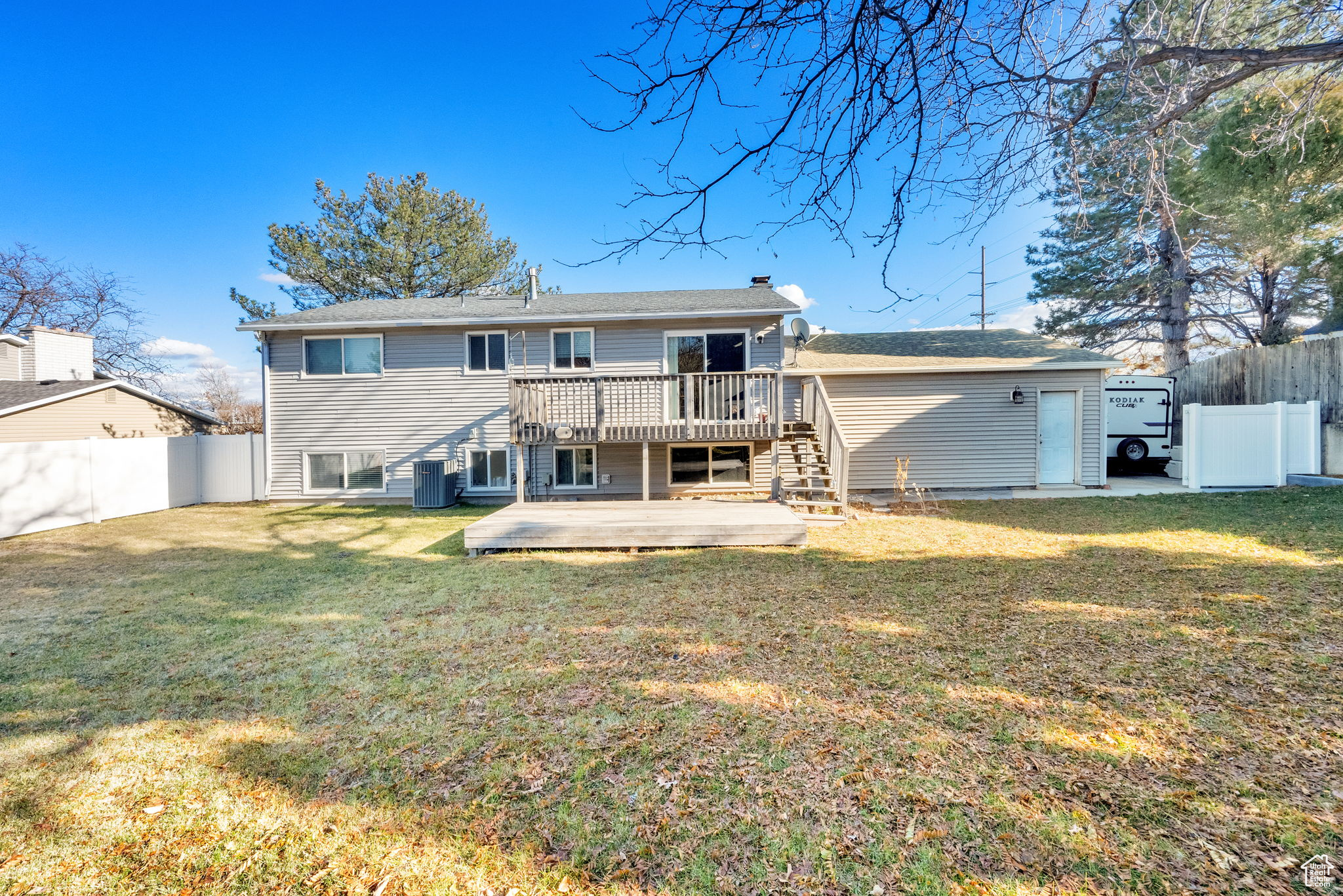 Back of house with a lawn, a wooden deck, and central AC