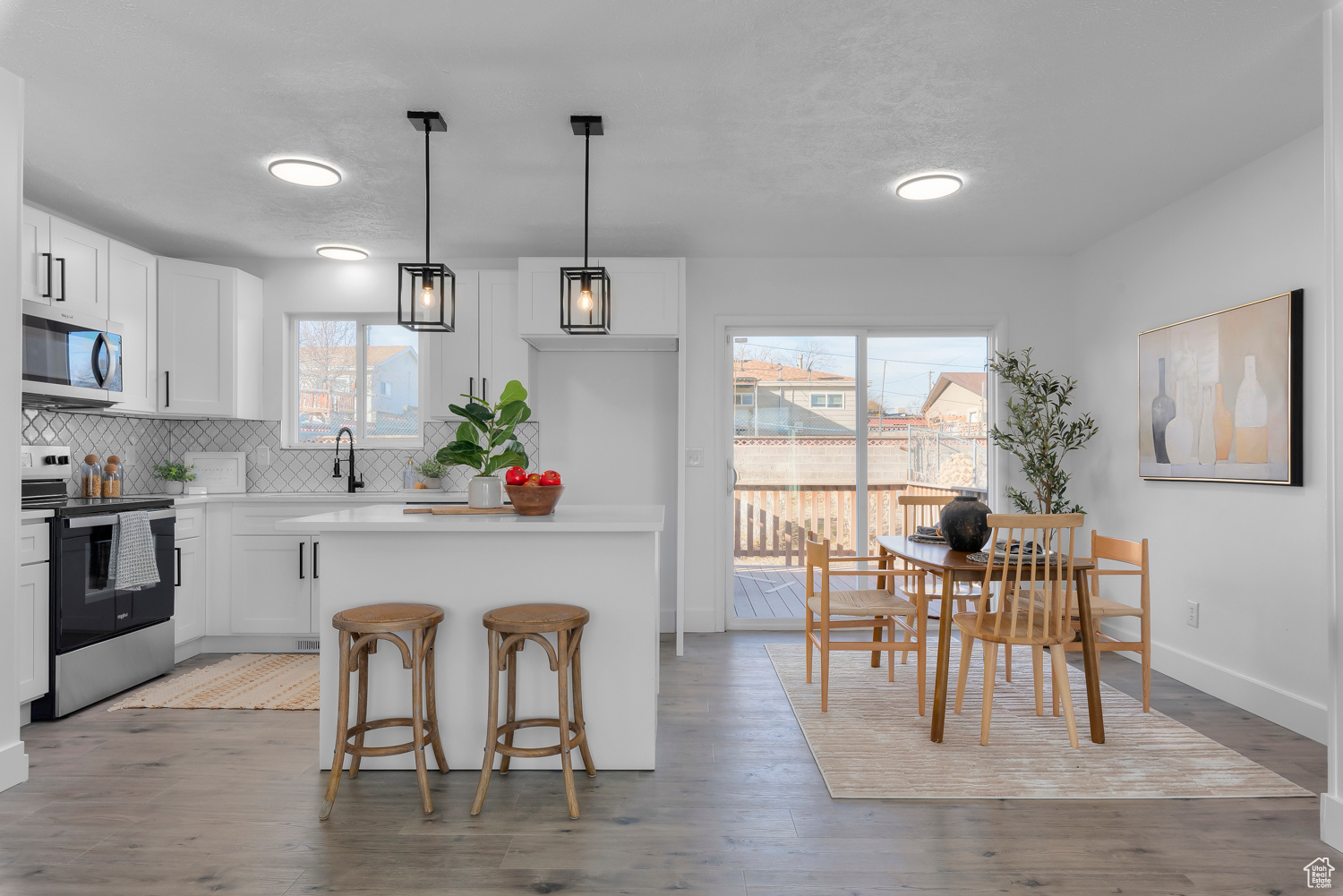 Kitchen featuring decorative light fixtures, stainless steel appliances, white cabinetry, and plenty of natural light