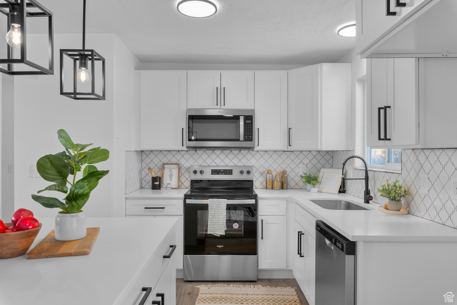 Kitchen featuring sink, white cabinetry, stainless steel appliances, and hanging light fixtures