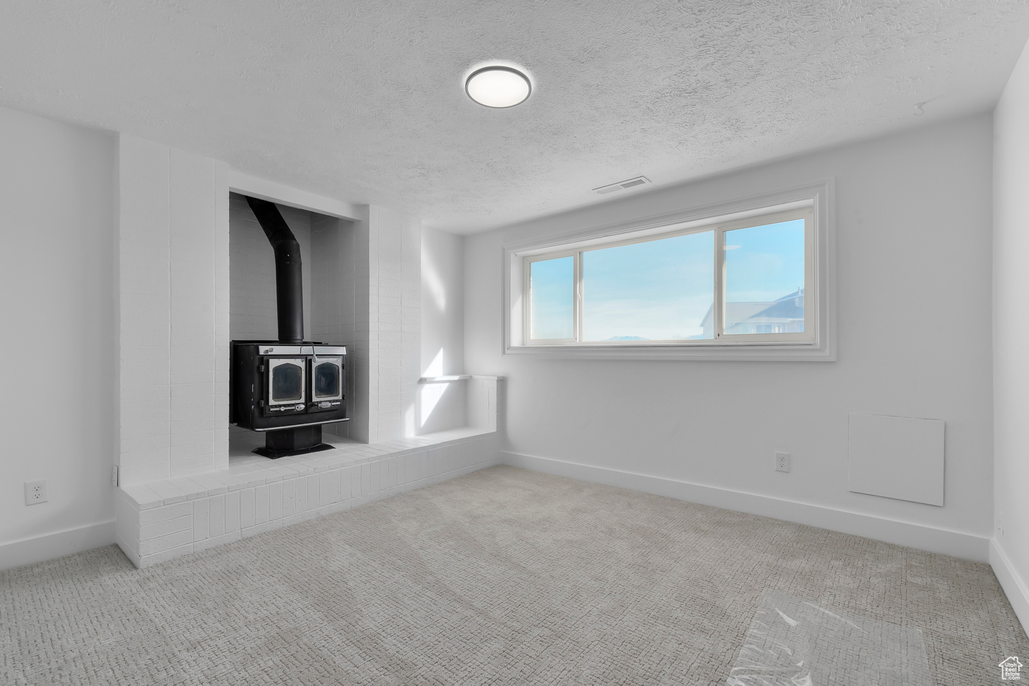 Unfurnished living room featuring a textured ceiling, light colored carpet, and a wood stove