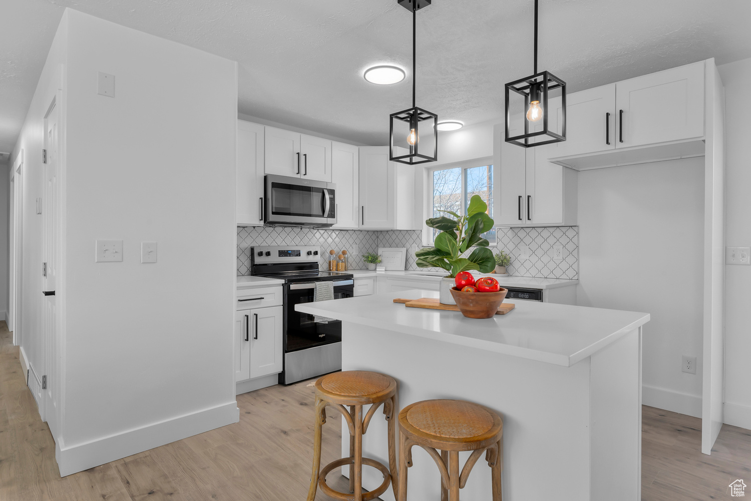 Kitchen featuring white cabinetry, hanging light fixtures, appliances with stainless steel finishes, and light hardwood / wood-style flooring