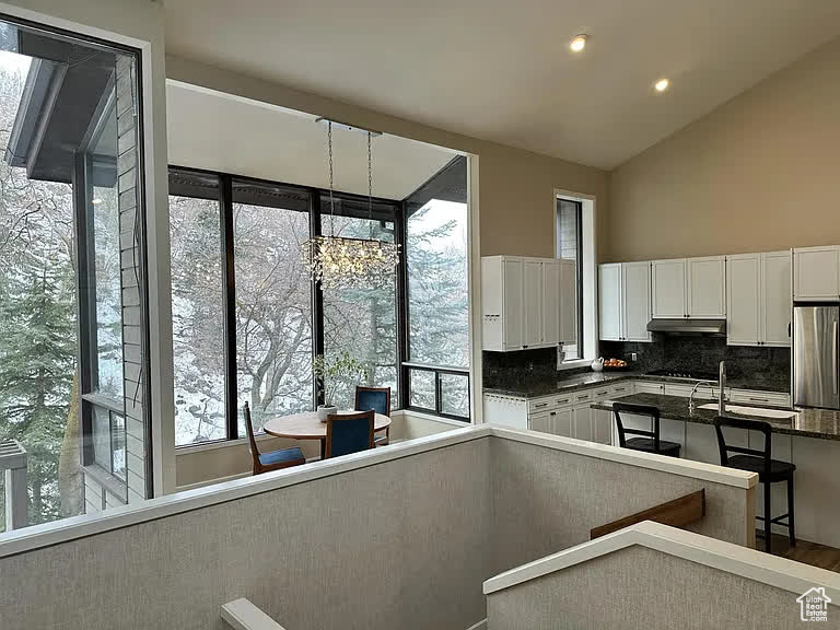 Kitchen featuring backsplash, vaulted ceiling, hardwood / wood-style flooring, stainless steel fridge, and white cabinetry