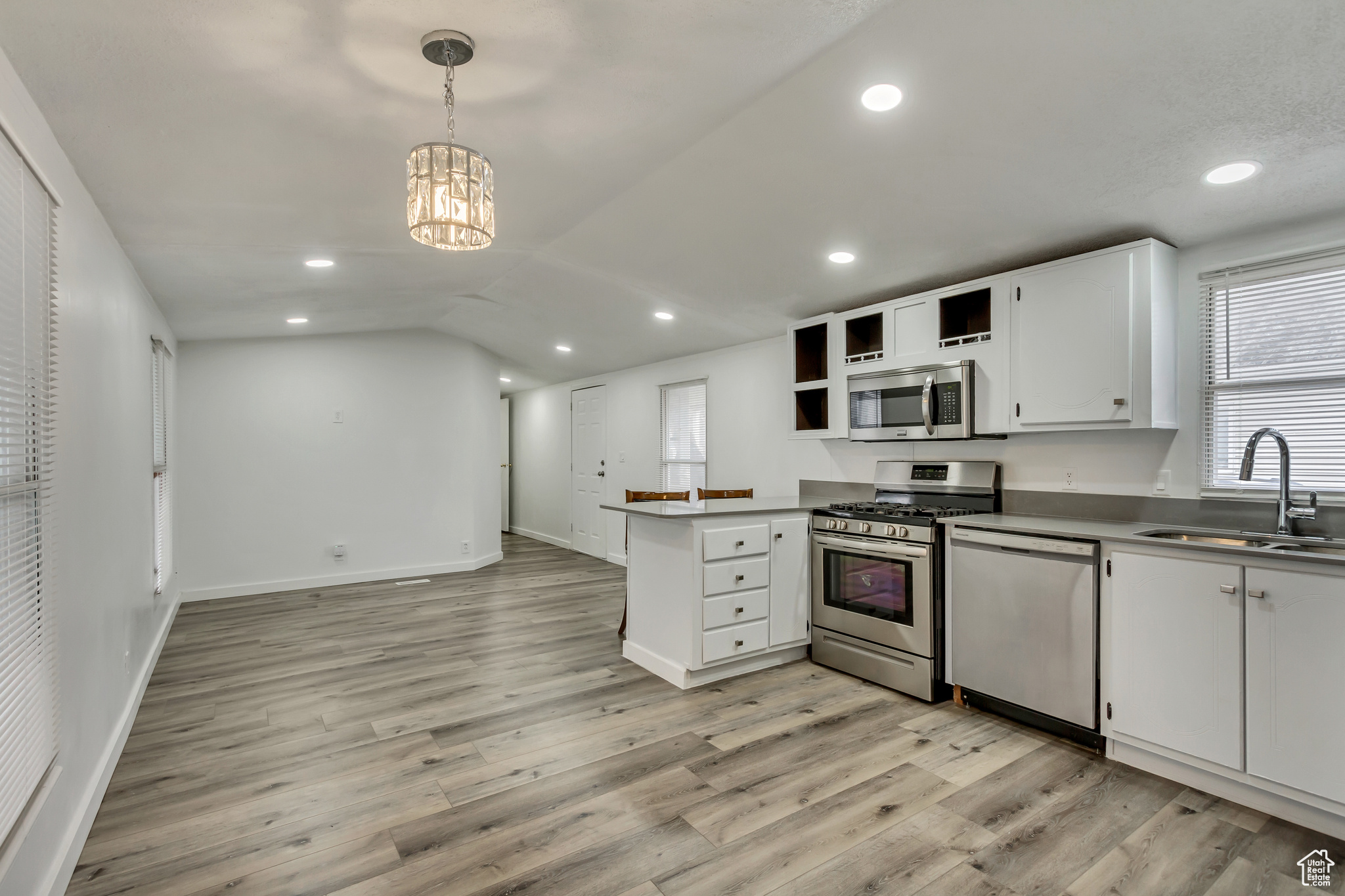 Kitchen featuring sink, kitchen peninsula, hanging light fixtures, white cabinetry, and stainless steel appliances