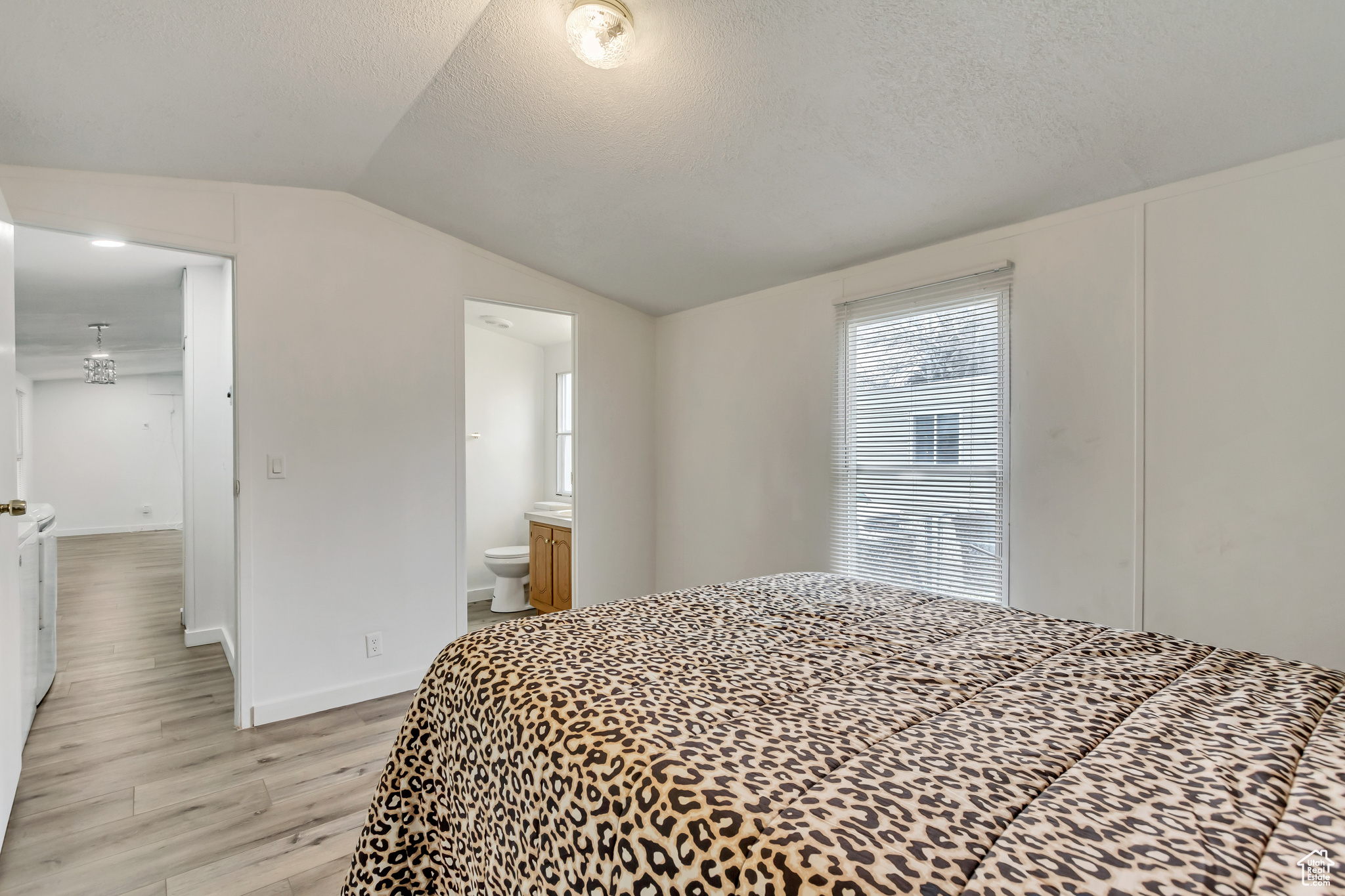 Bedroom featuring a textured ceiling, ensuite bath, light hardwood / wood-style flooring, and lofted ceiling