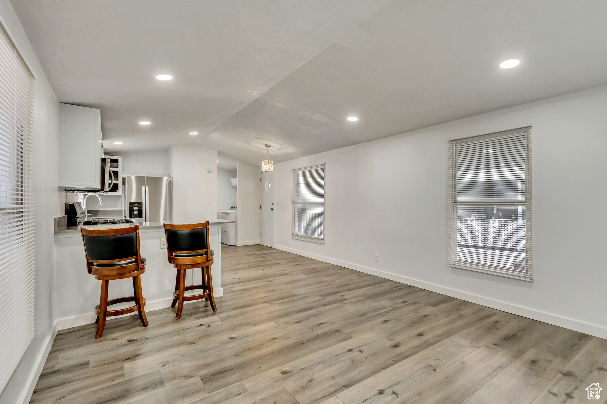 Kitchen with a kitchen breakfast bar, light wood-type flooring, stainless steel appliances, white cabinetry, and plenty of natural light